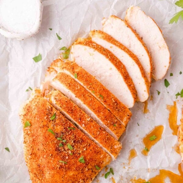 Sliced, seasoned baked chicken breast on parchment paper, garnished with chopped herbs.