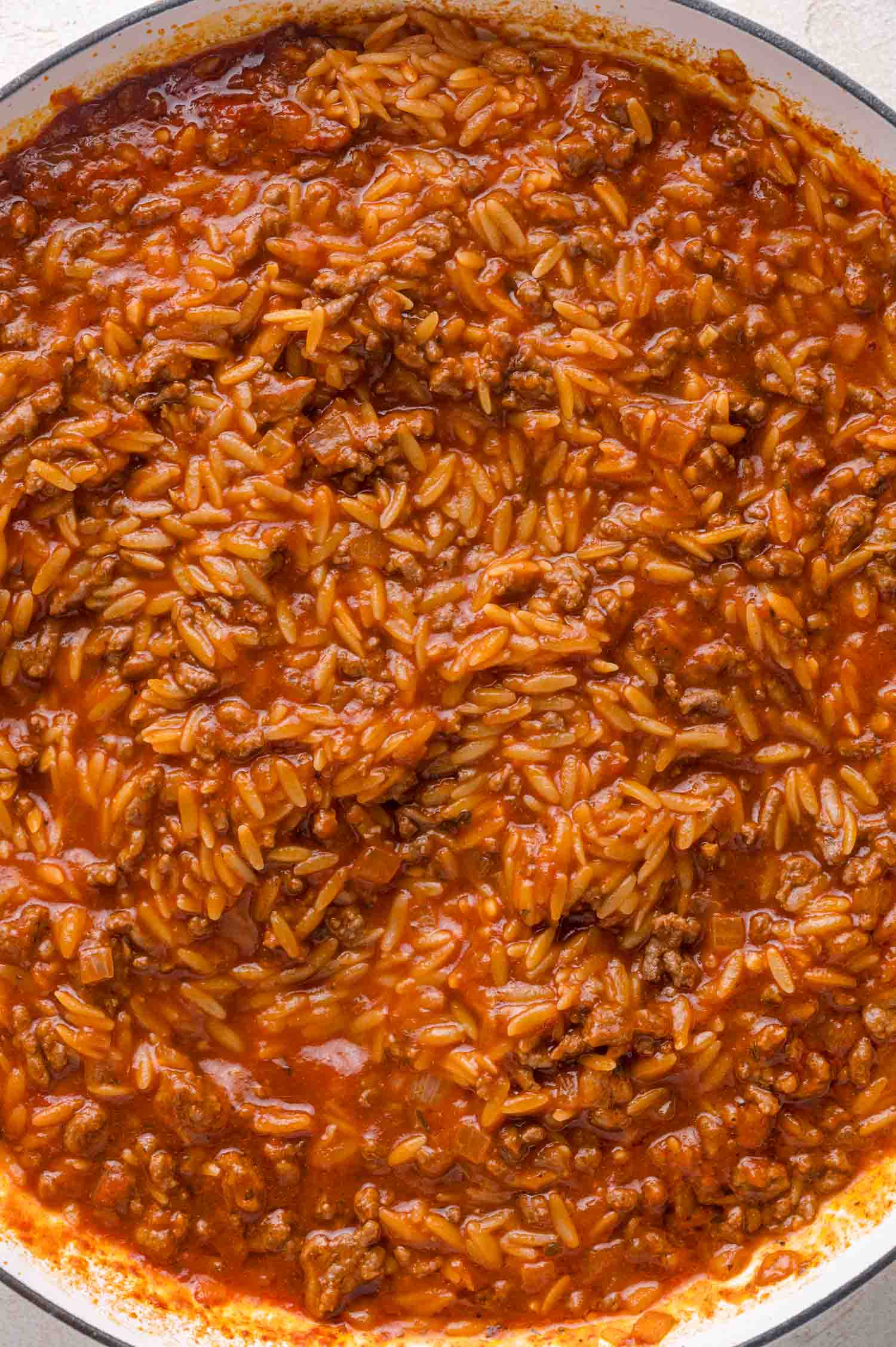 A close-up of a pan filled with cooked ground beef, orzo, and tomato sauce mixed together.