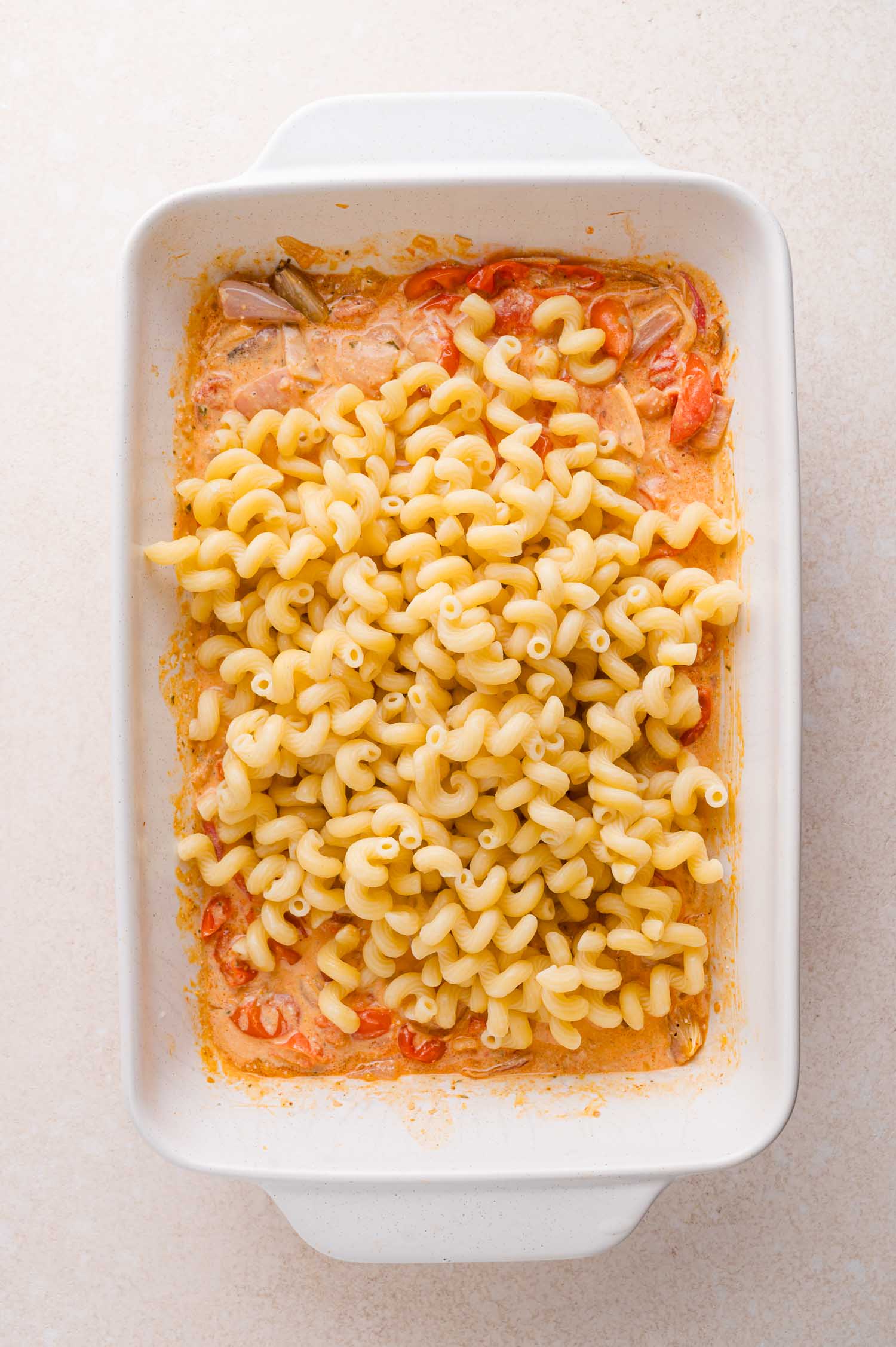 Baked pasta casserole in a white dish, with cooked cavatappi noodles on top of a creamy tomato and cheese sauce.