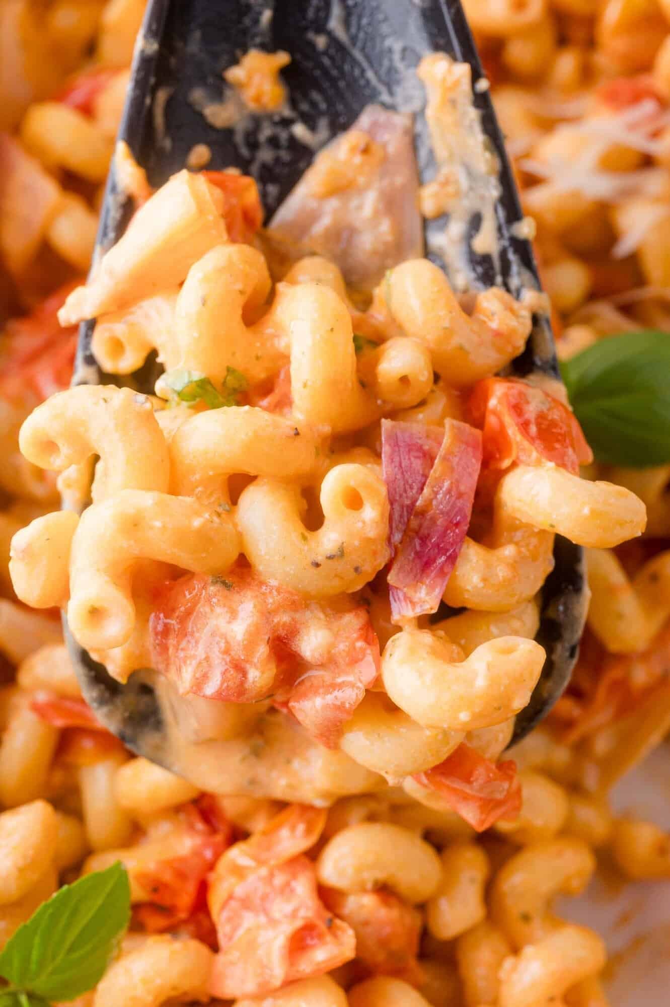 A close-up of a spoonful of creamy Boursin pasta with diced tomatoes and herbs.