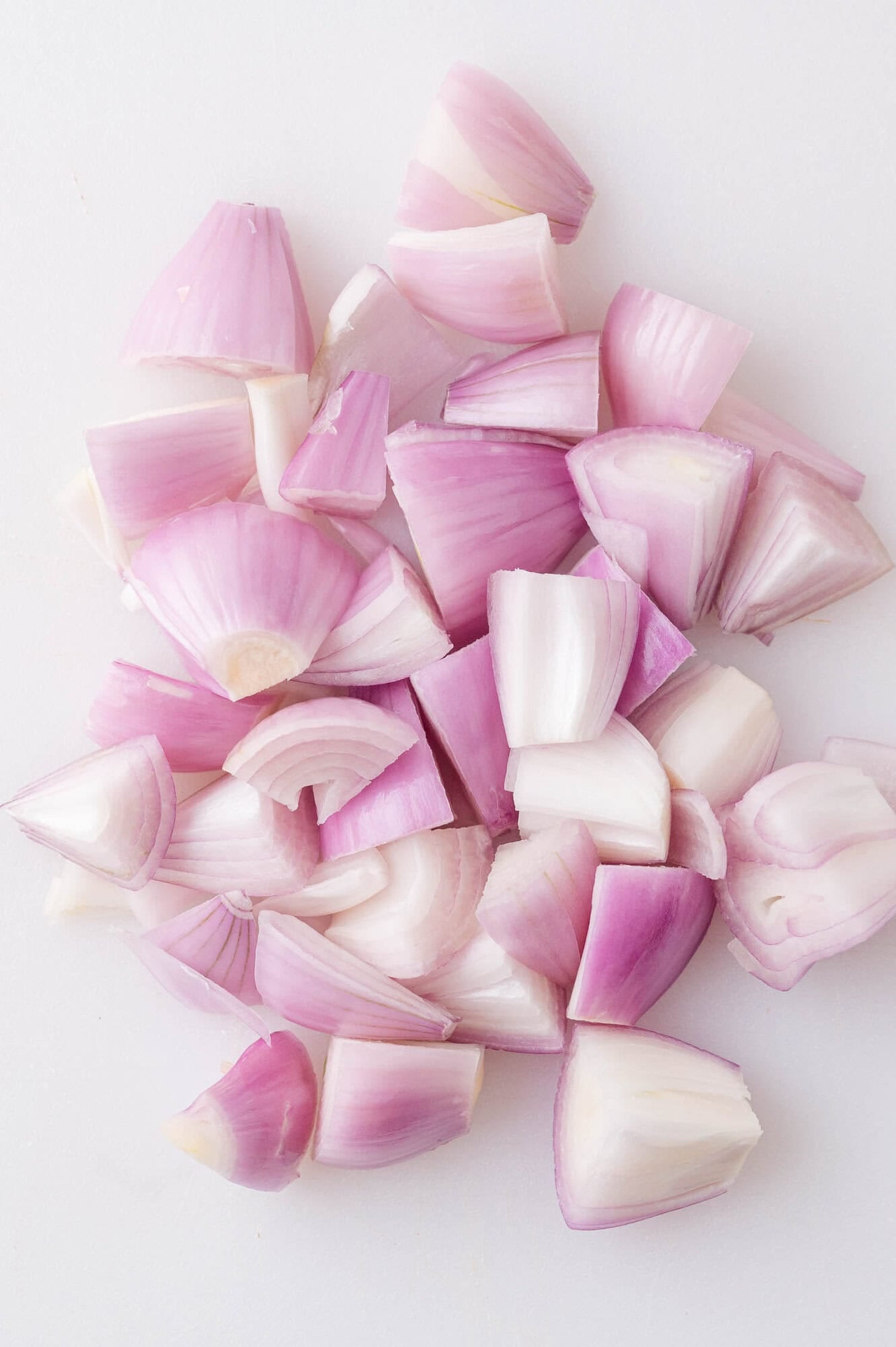 Chopped red onions in uneven pieces on a white surface.