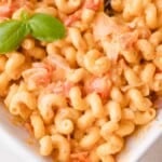 A close-up of creamy Boursin pasta with diced tomatoes, melted cheese, and a sprig of fresh basil on top.