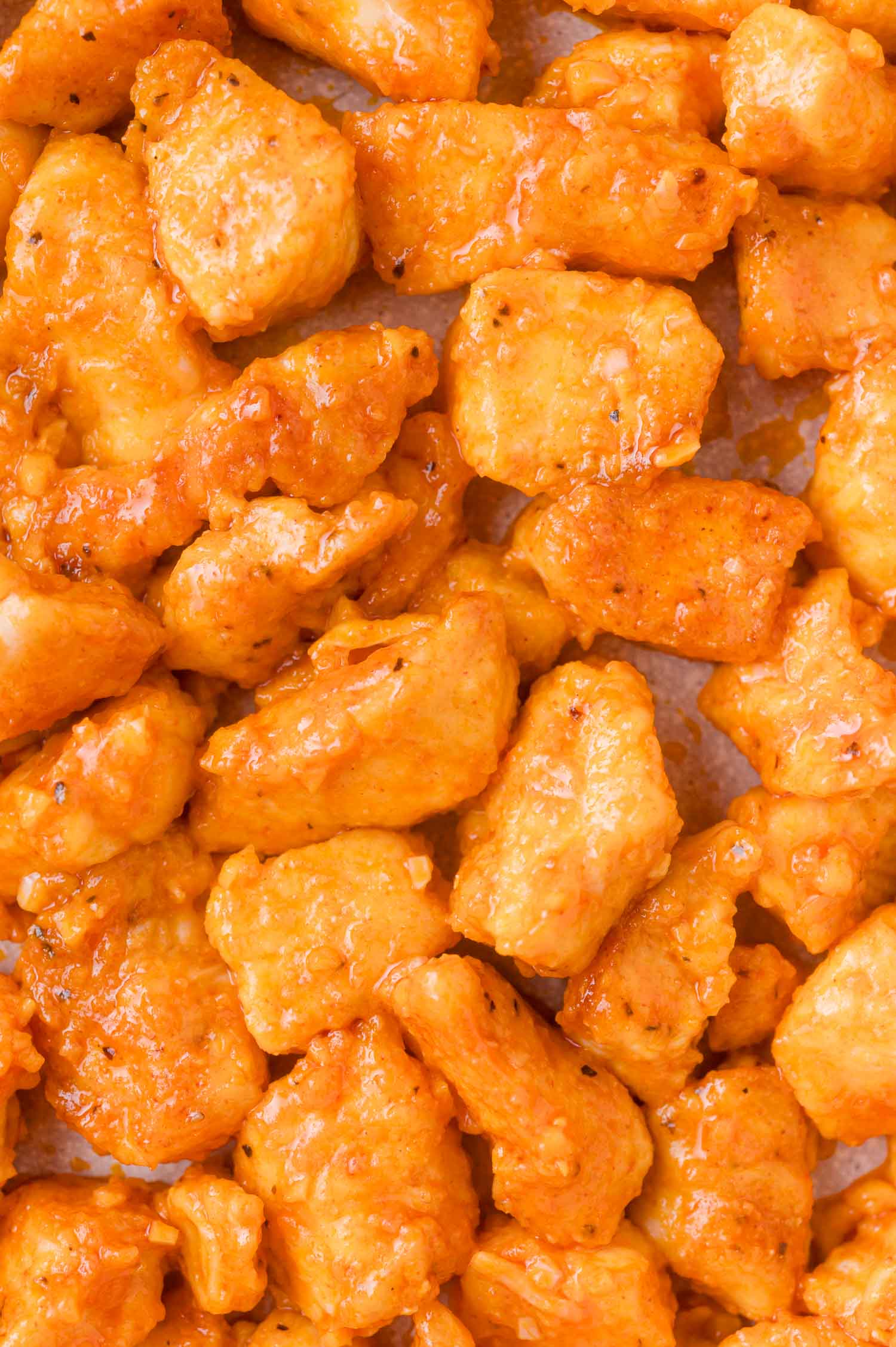 Close-up view of golden, sauced chicken pieces on a sheet, showing texture and seasoning.
