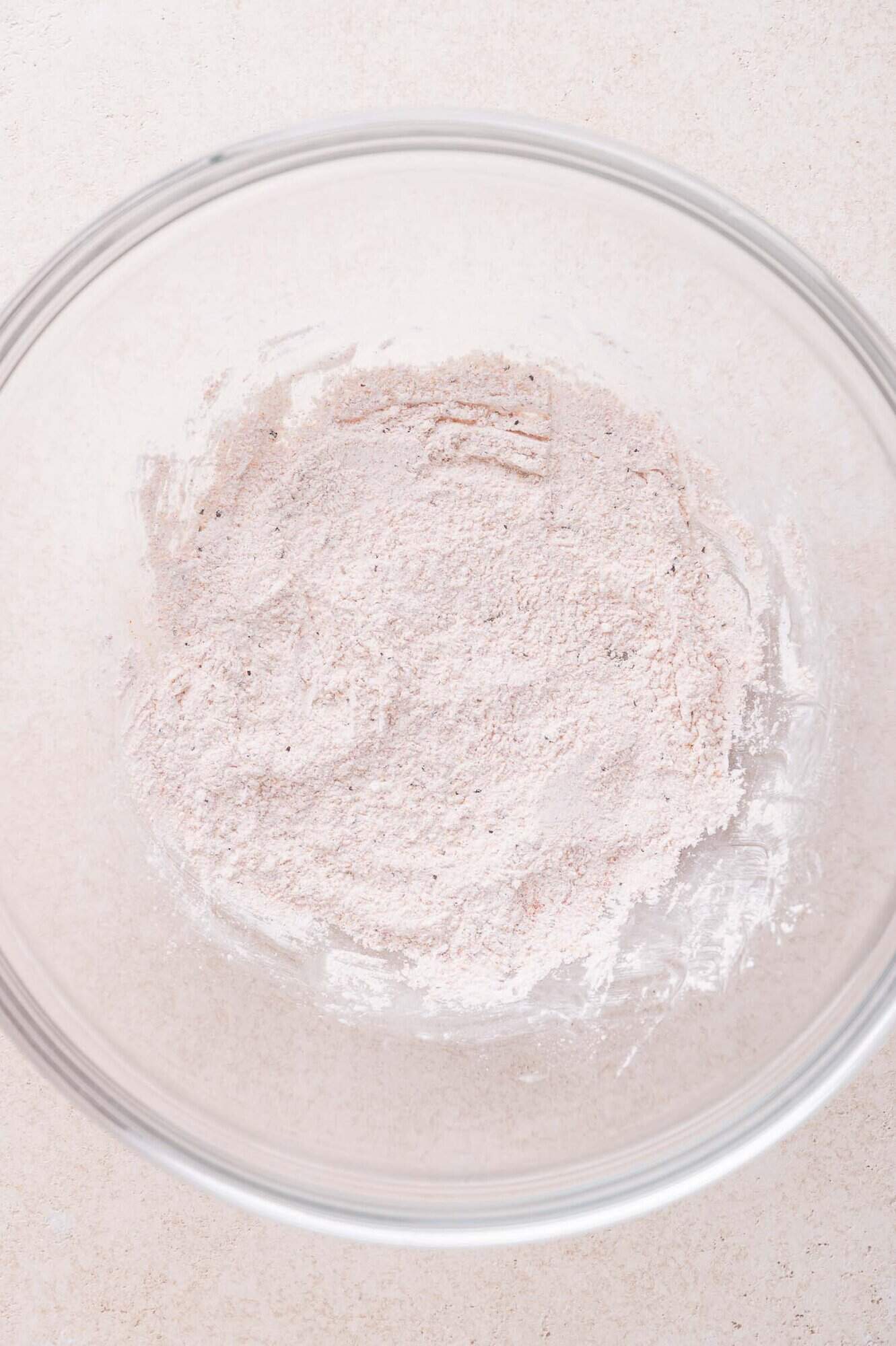A clear glass bowl containing a mixture of dry spices and cornstarch sits on a light-colored surface.