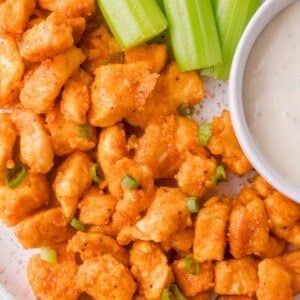Plate of buffalo chicken bites garnished with chopped green onions, served with celery sticks and a cup of ranch dressing.