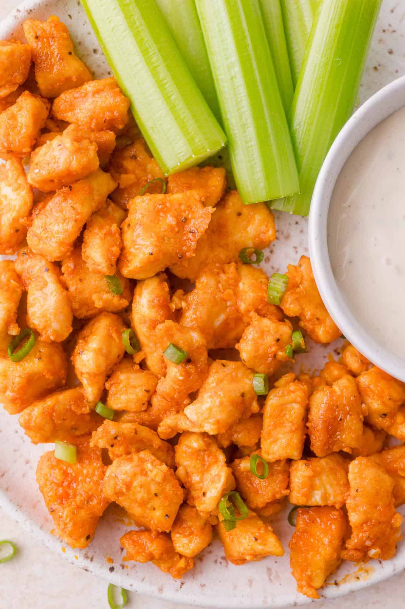 Plate of buffalo chicken bites with green onions, celery sticks, and a bowl of ranch dipping sauce.