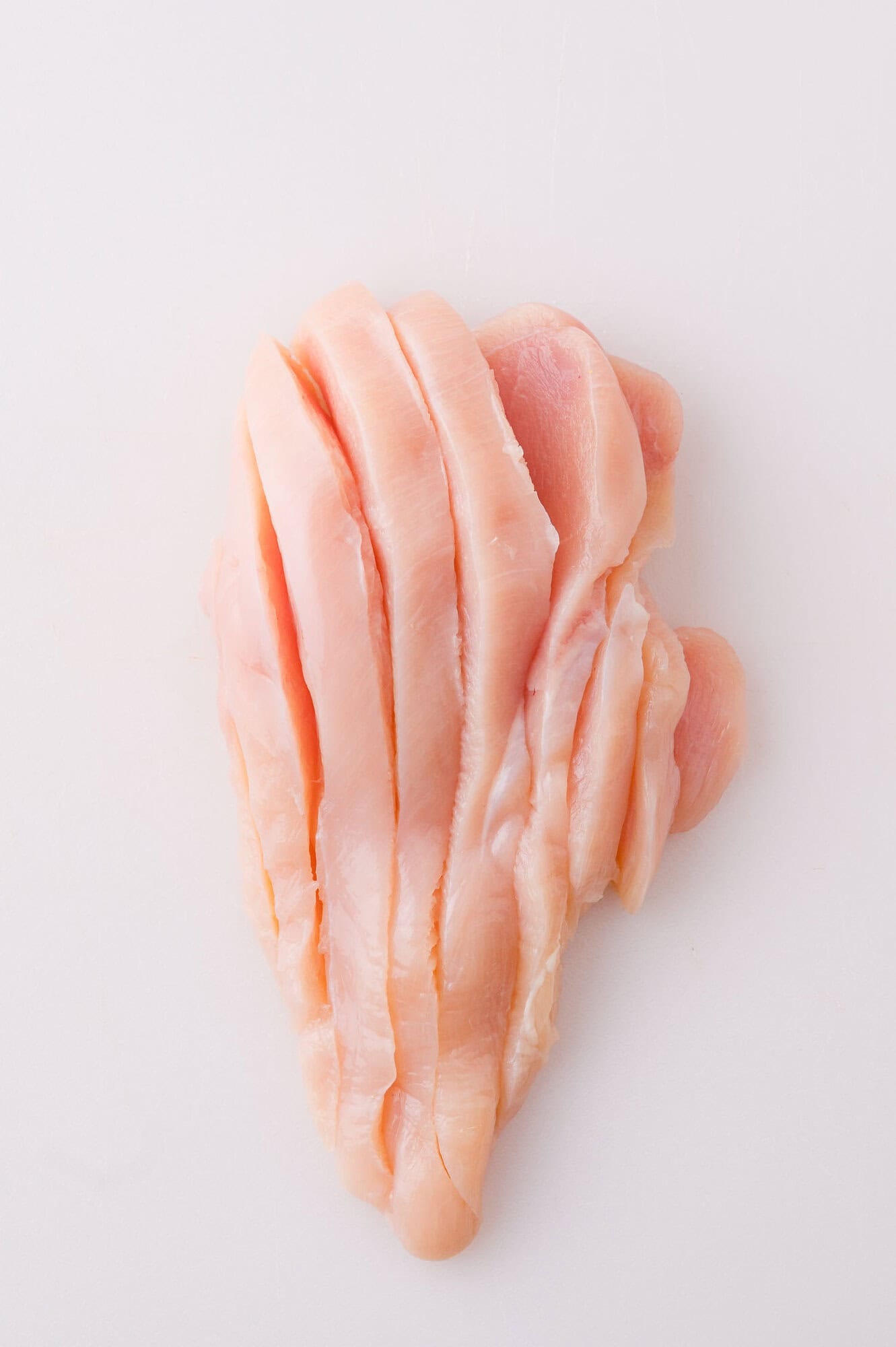 Raw, boneless chicken breast sliced into strips on a white surface.