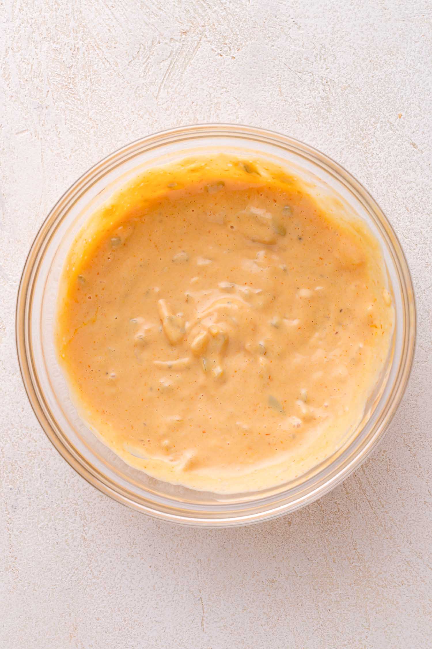 A glass bowl filled with creamy, orange-colored Big Mac sauce with visible small chunks, placed on a light-colored surface.