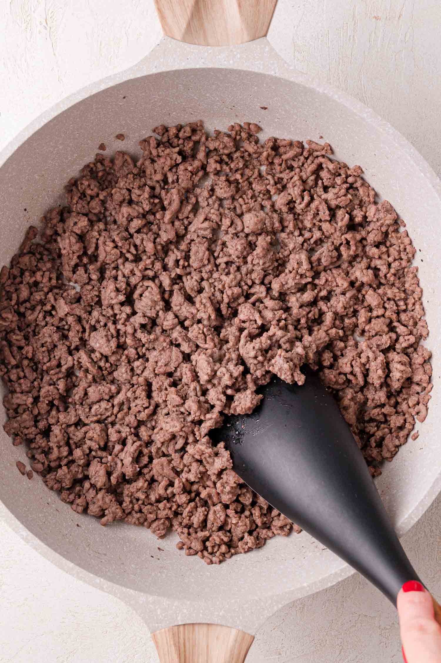Cooked ground beef being stirred in a white skillet with a black spatula.