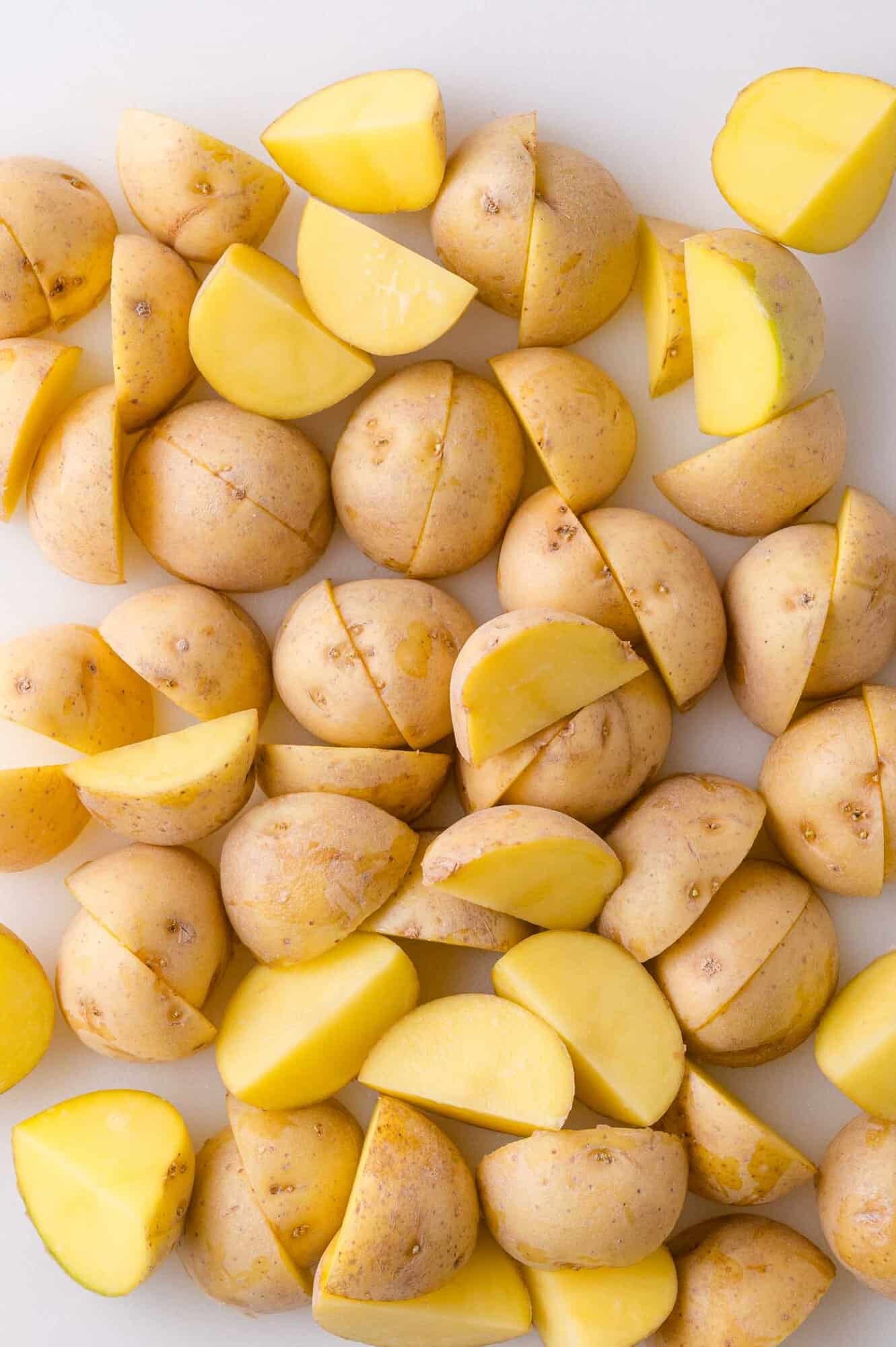 Halved and quartered yellow potatoes with skins on, arranged on a white surface.