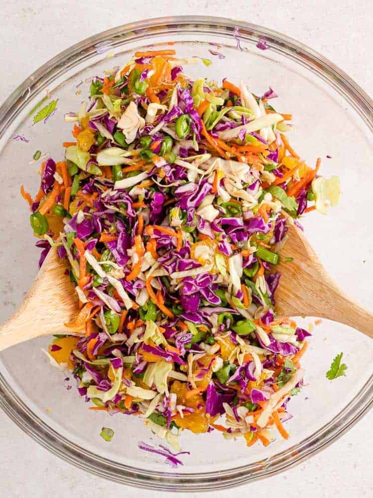 Cabbage salad being mixed with two spoons.