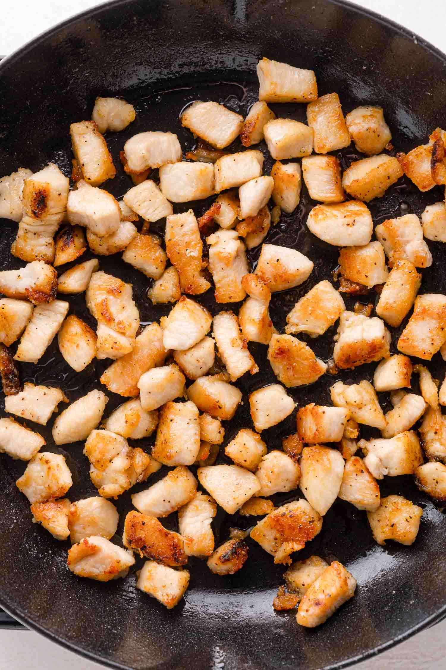 Diced pieces of cooked, browned chicken breast in a black frying pan.