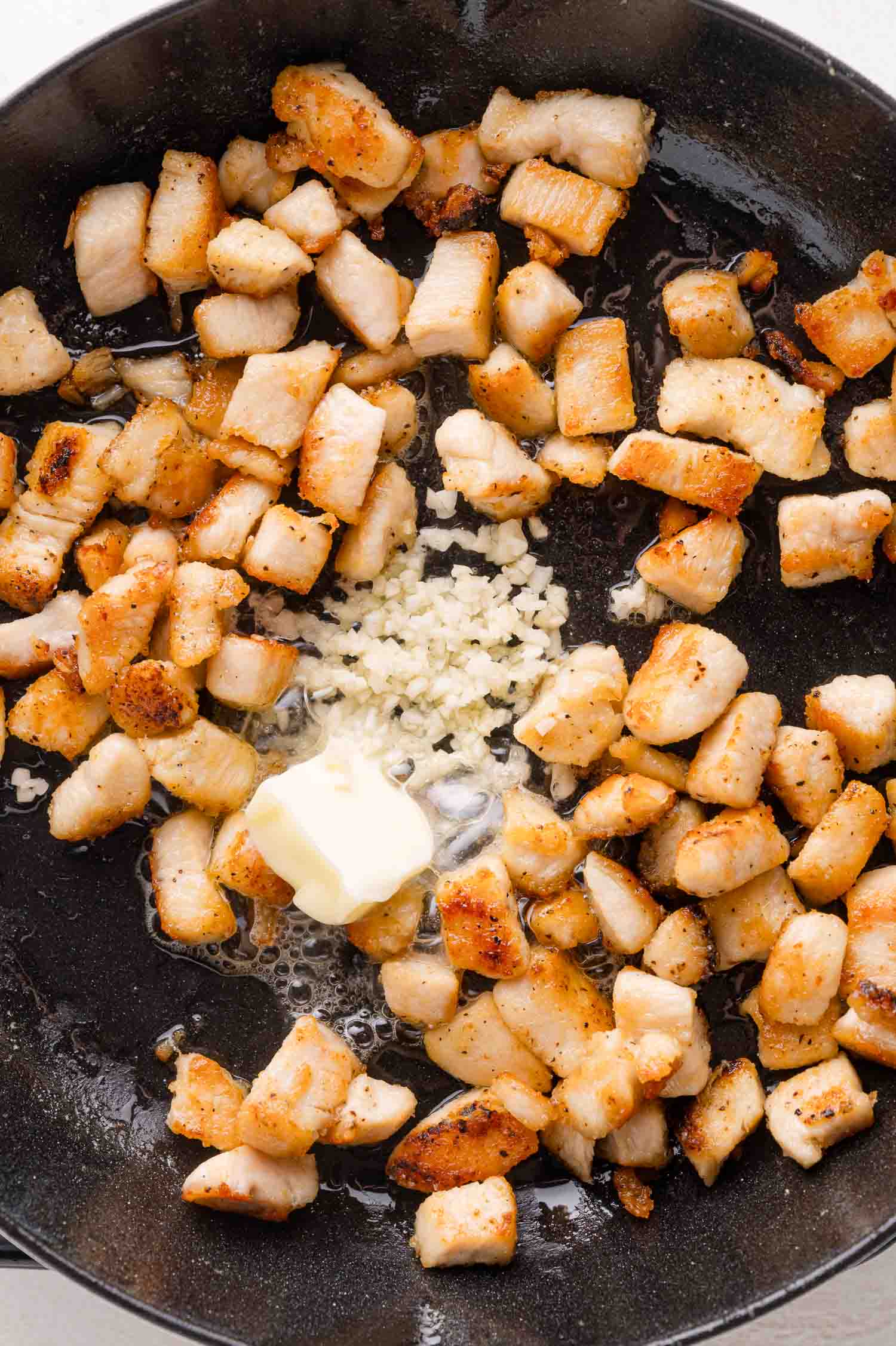 Diced cooked chicken pieces, minced garlic, and a pat of butter in a black skillet.