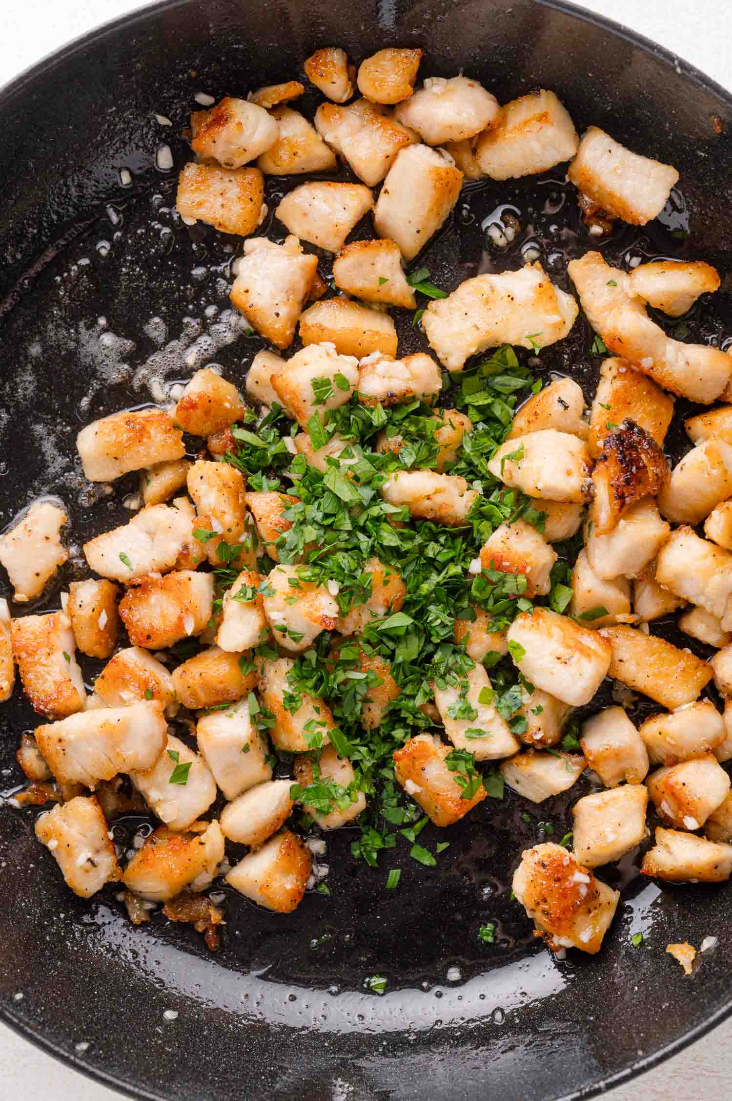 Cooked diced chicken pieces in a skillet, garnished with chopped fresh herbs in the center.