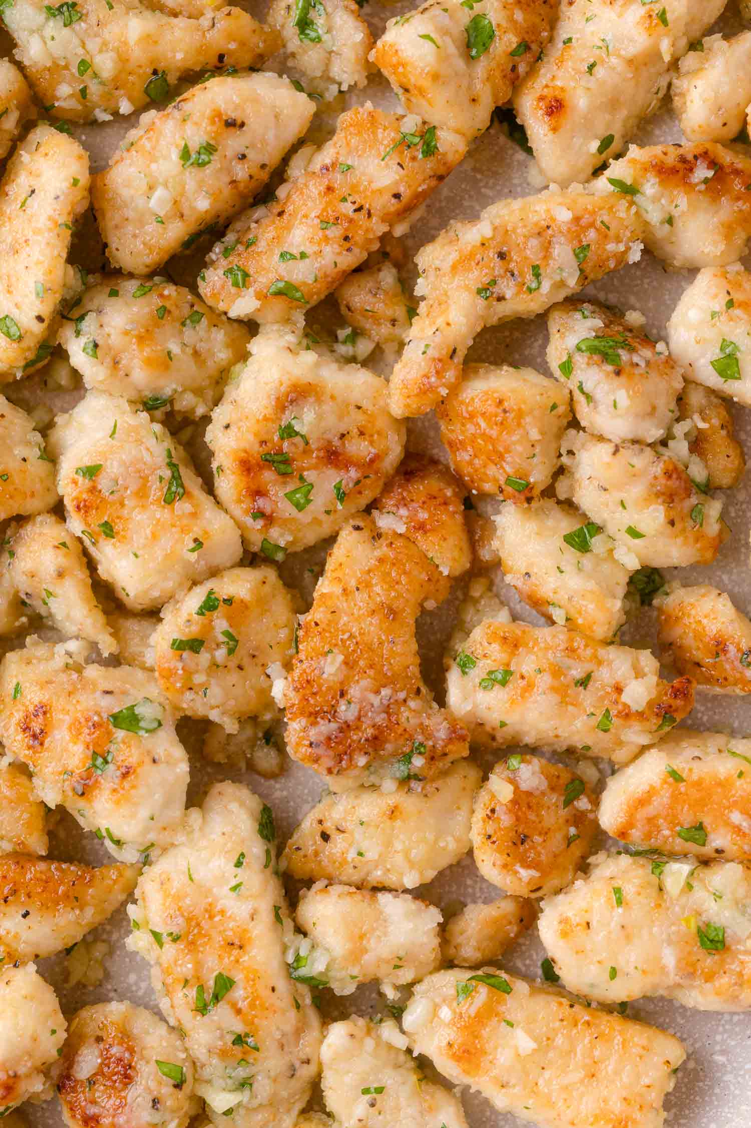 Close-up of cooked, golden-brown chicken pieces garnished with chopped herbs on a flat surface.