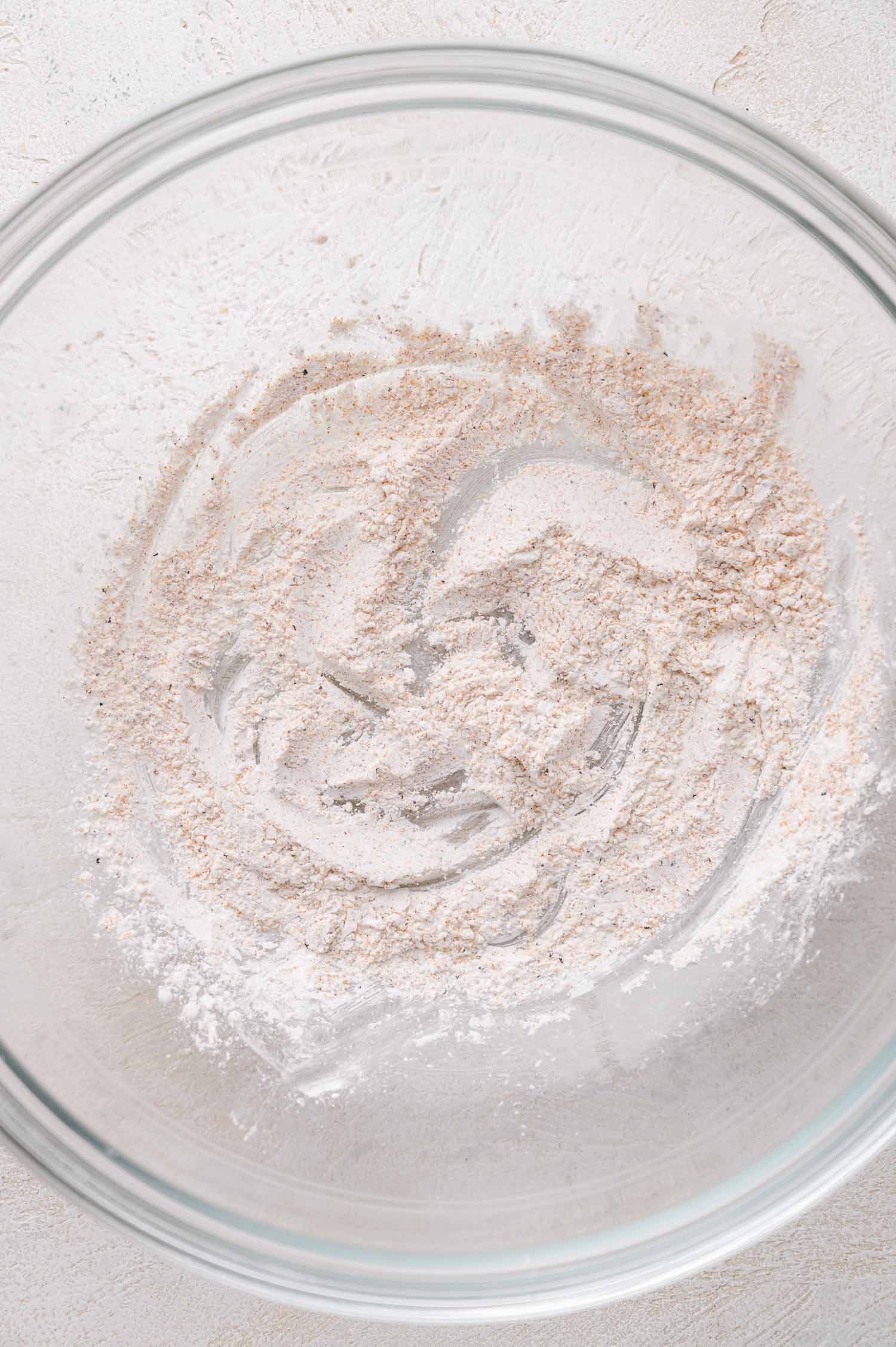 A clear glass mixing bowl contains a small amount of cornstarch on the bottom, lightly spread across the surface.