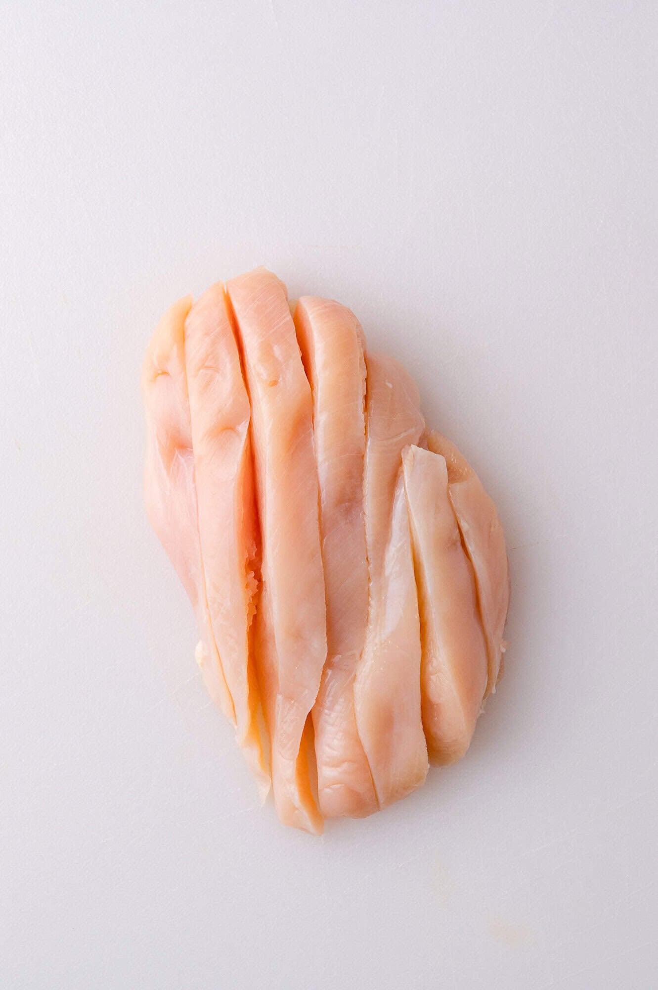 Raw chicken breast sliced into strips on a white cutting board.