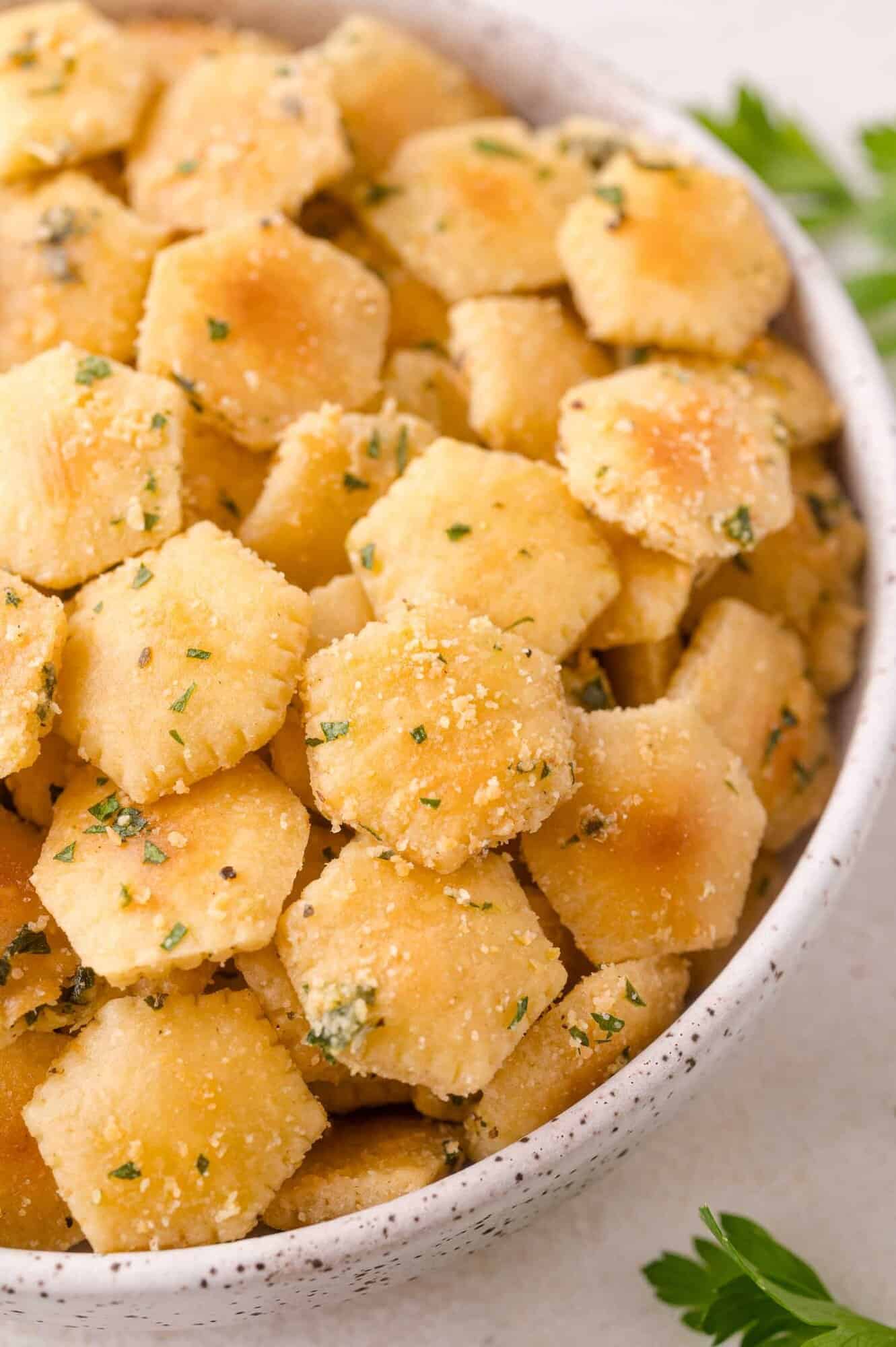 Bowl filled with seasoned oyster crackers coated in herbs and spices, with parsley garnish visible nearby.