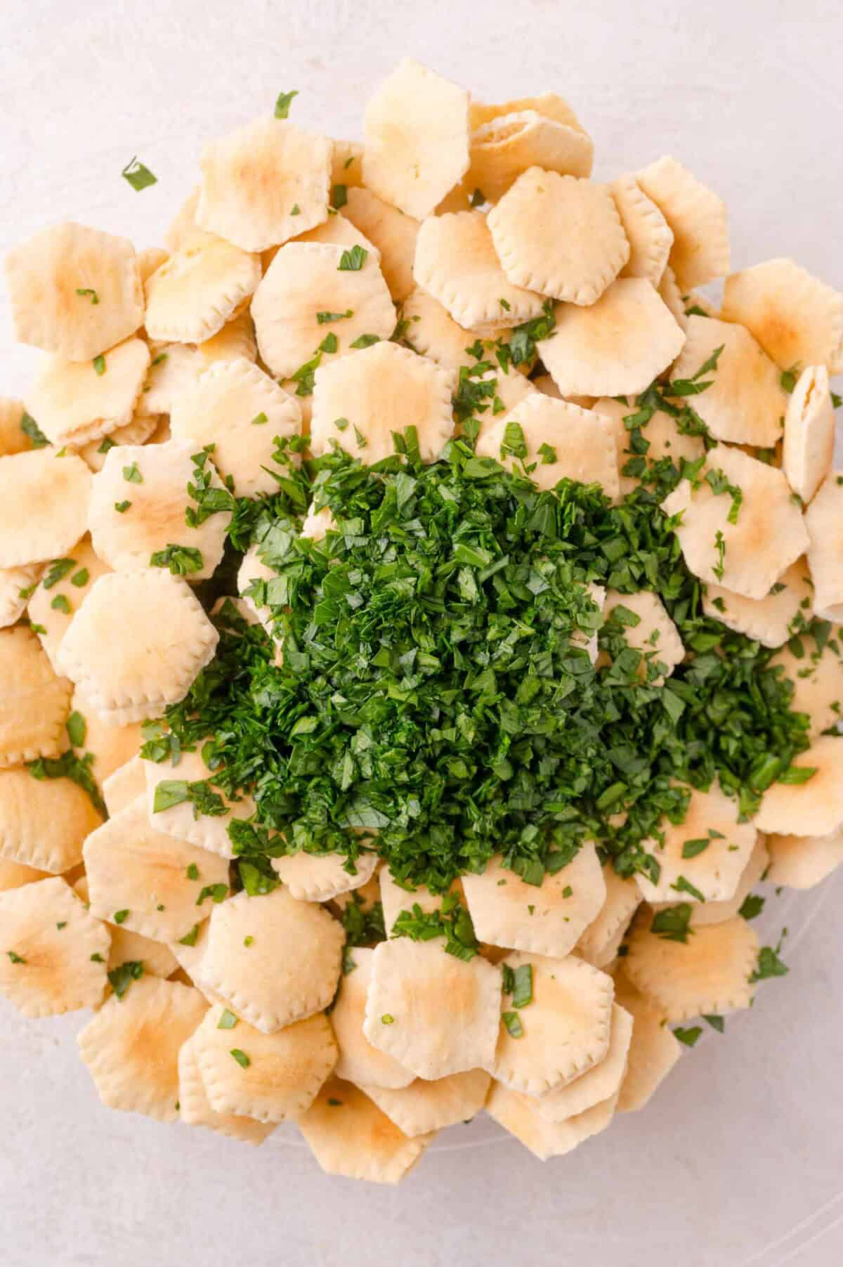 A pile of oyster crackers topped with a generous amount of freshly chopped parsley on a light surface.