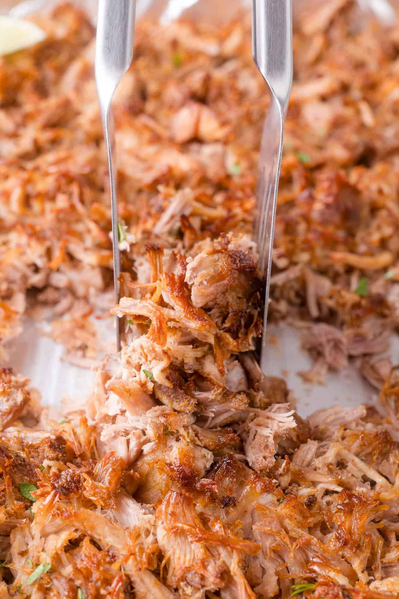 Two forks shredding cooked, crispy pulled pork on a white surface.