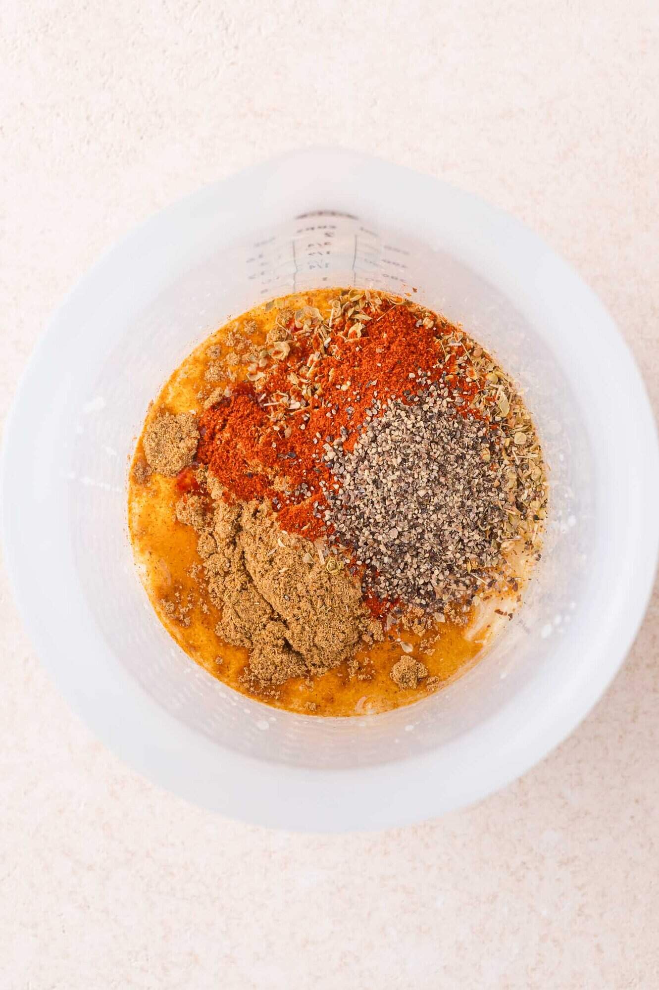 A mixing bowl containing ground spices, black pepper, and liquid ingredients arranged in separate piles before mixing.