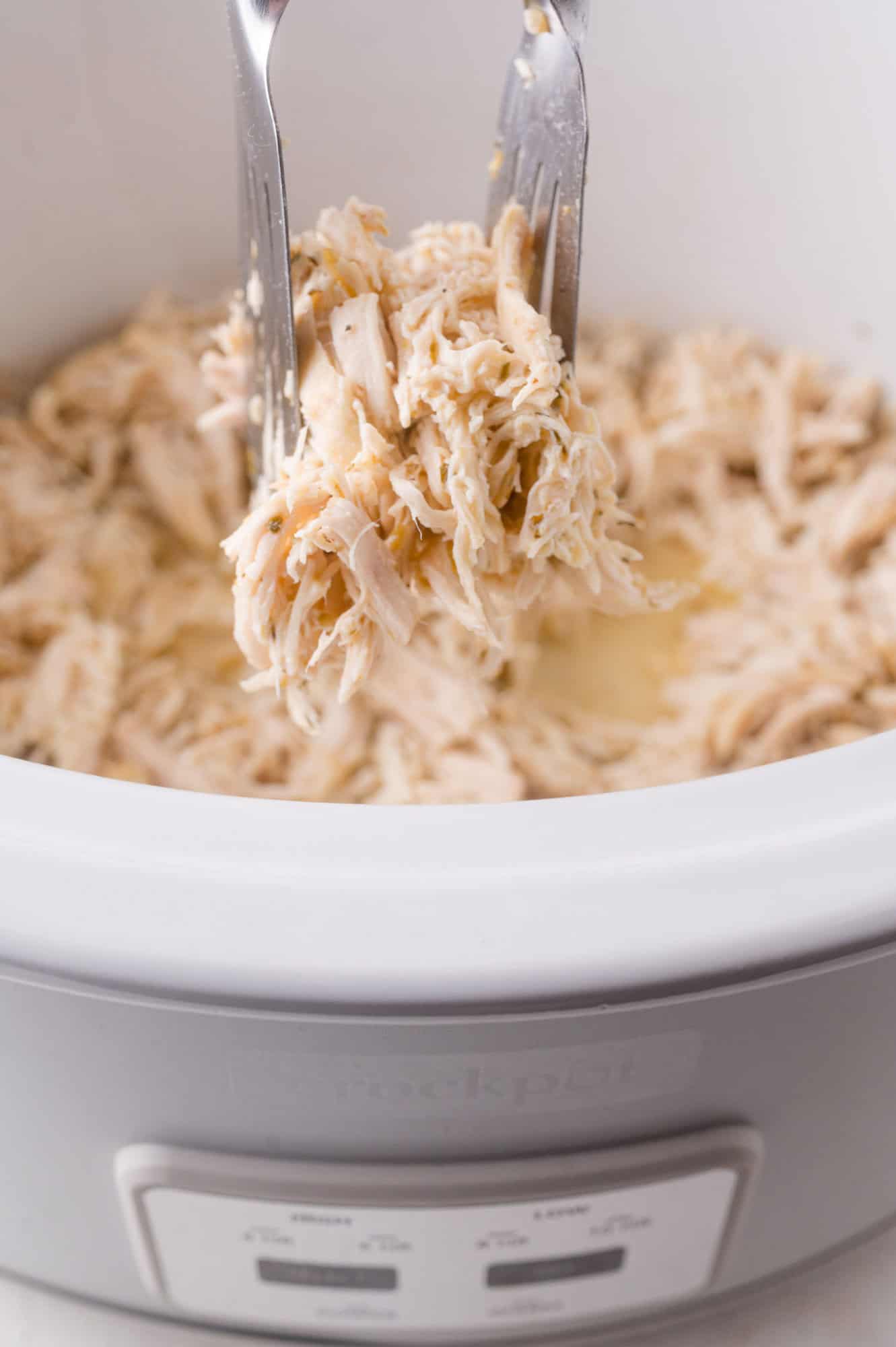 Shredded chicken being pulled apart with two forks inside a slow cooker.