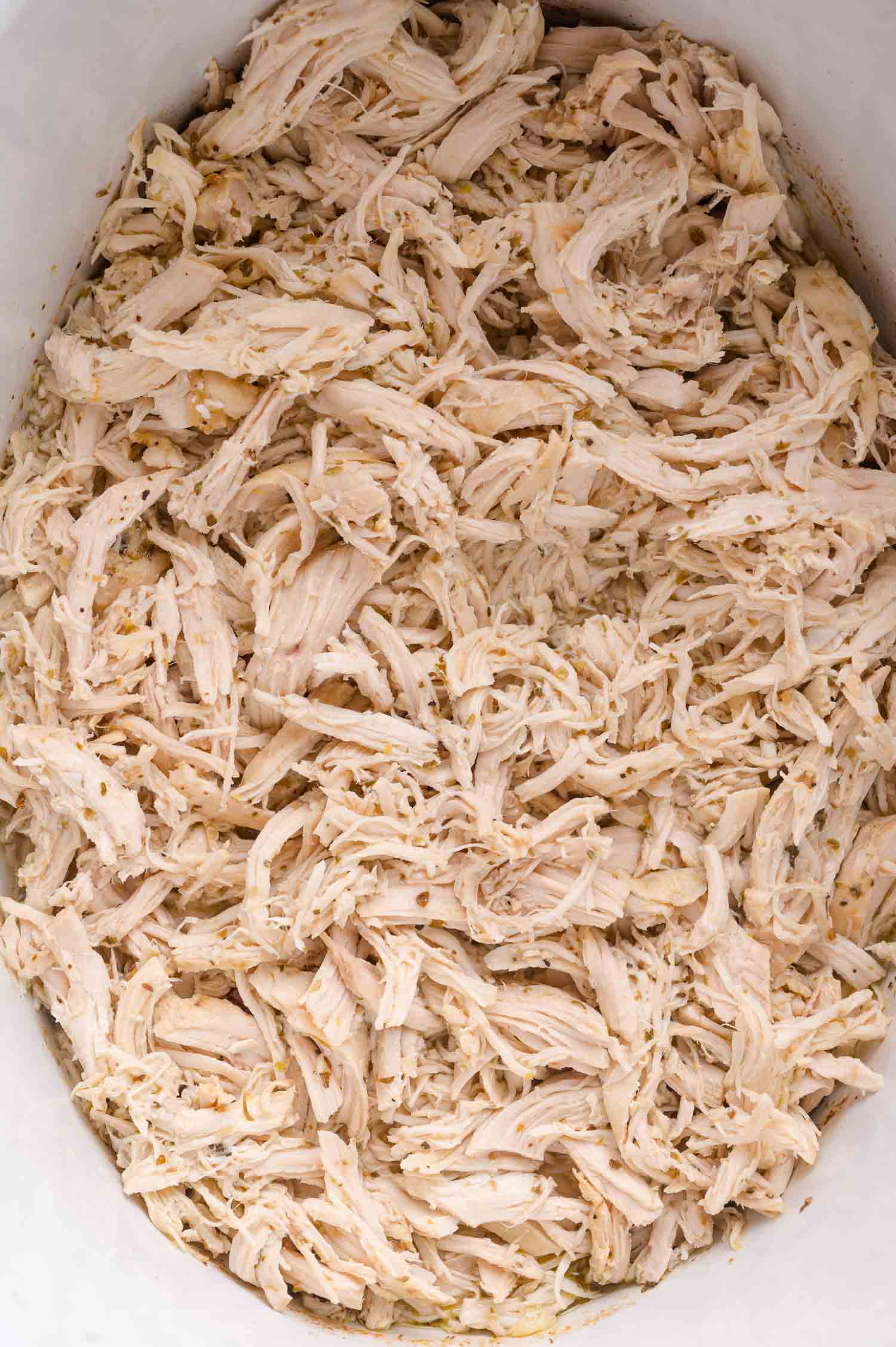 Shredded cooked chicken breast spread out in a white dish.
