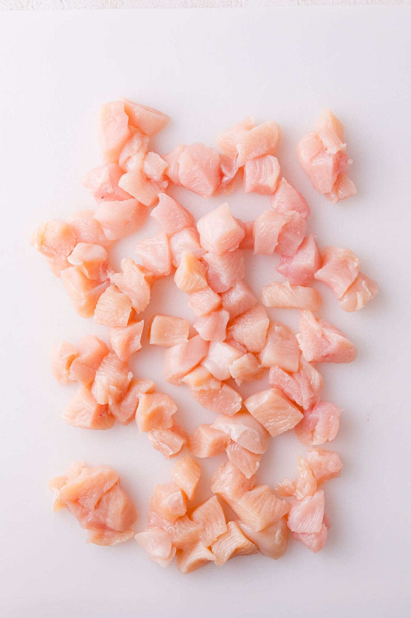Raw chicken breast cut into small, evenly sized cubes arranged on a white cutting board.