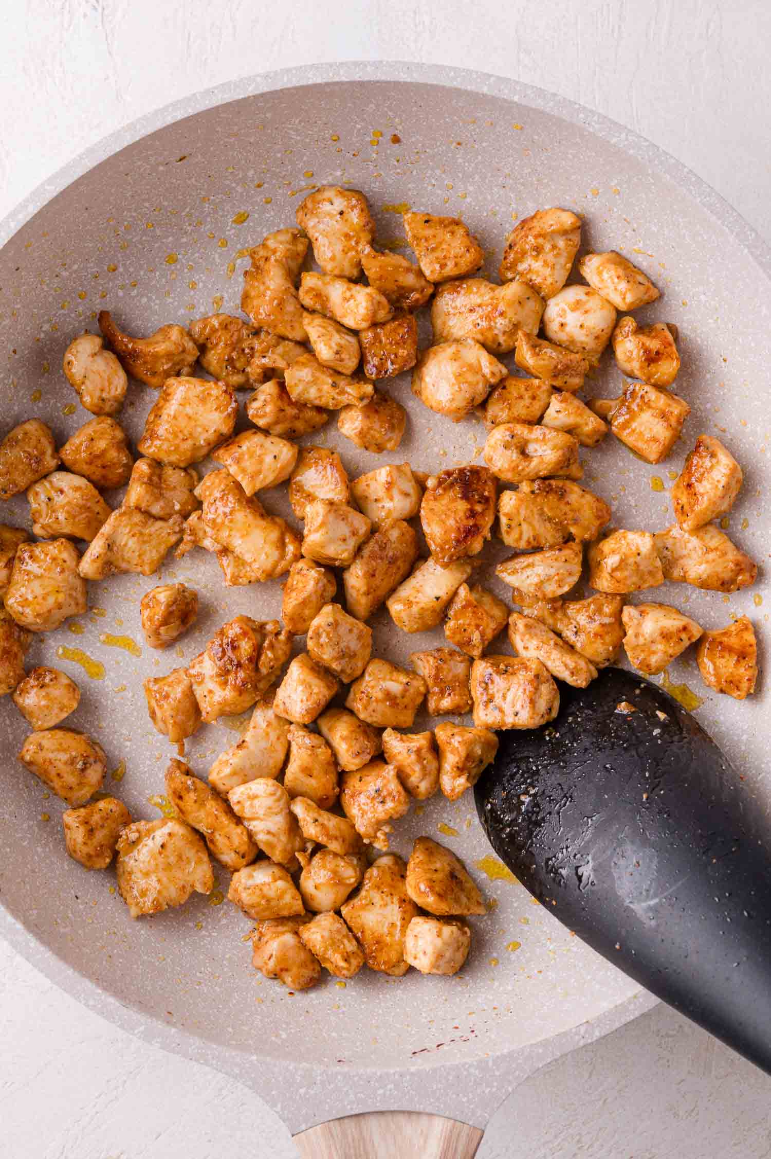 Cooked, seasoned chicken breast pieces in a frying pan with a black spatula.