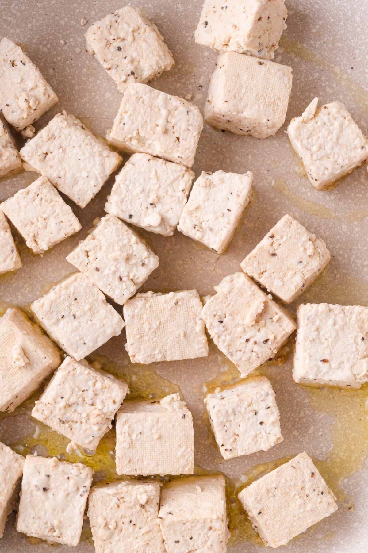 Cubed tofu pieces seasoned with pepper and scattered on a light-colored surface with a drizzle of oil.