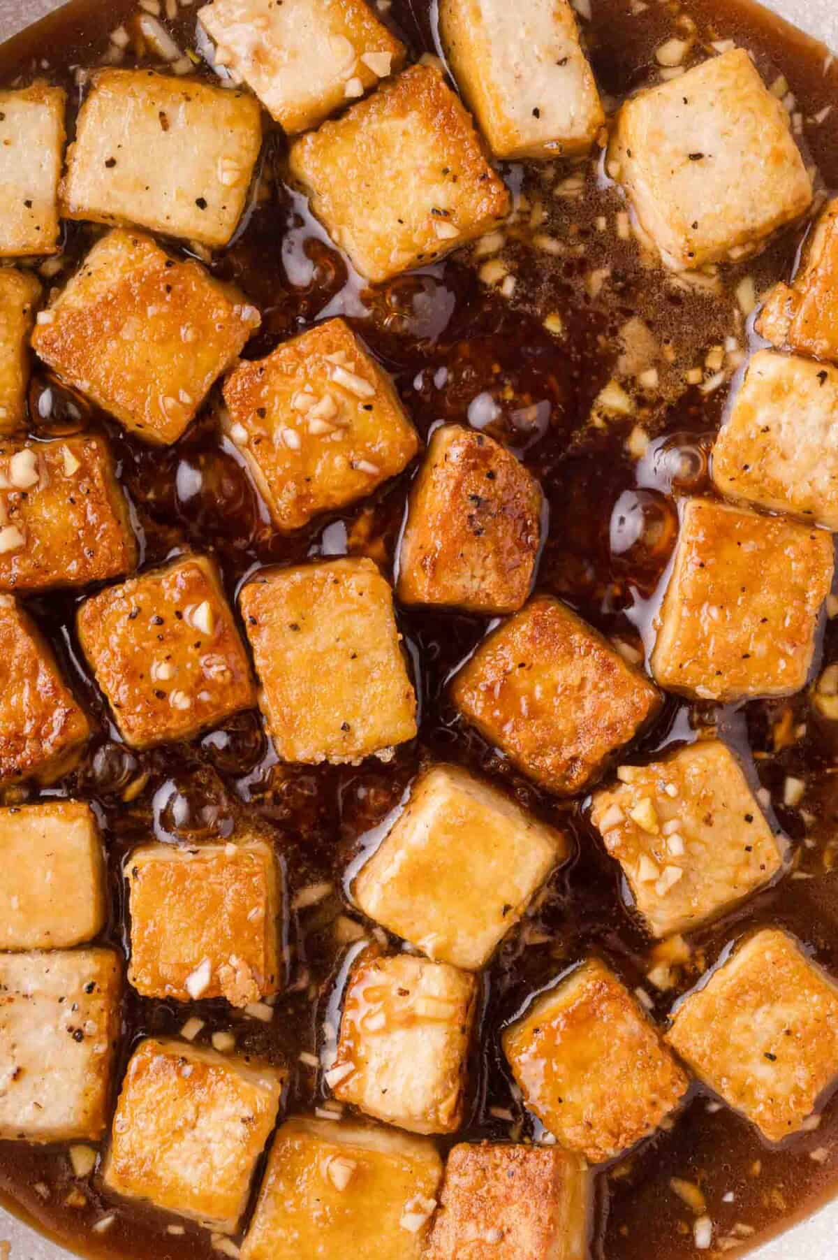 Golden brown tofu cubes in a dark, garlicky sauce, shown from above.