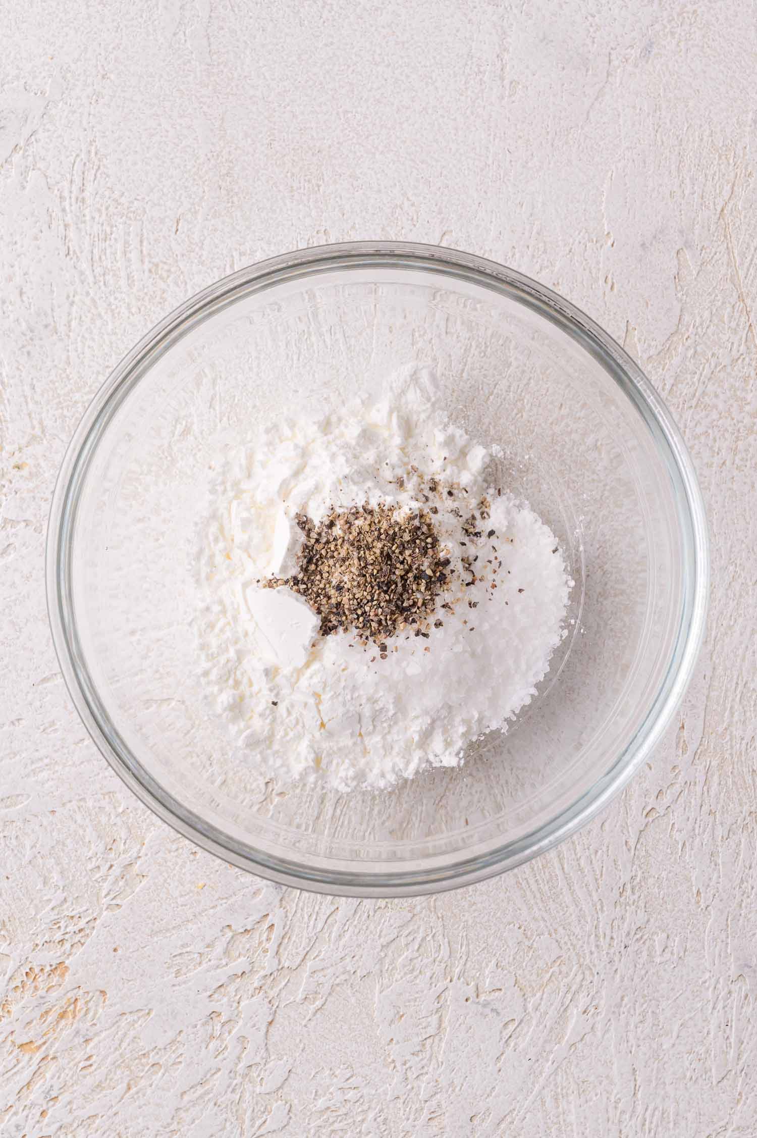 A glass bowl containing a mixture of cornstarch and a small amount of ground black pepper.