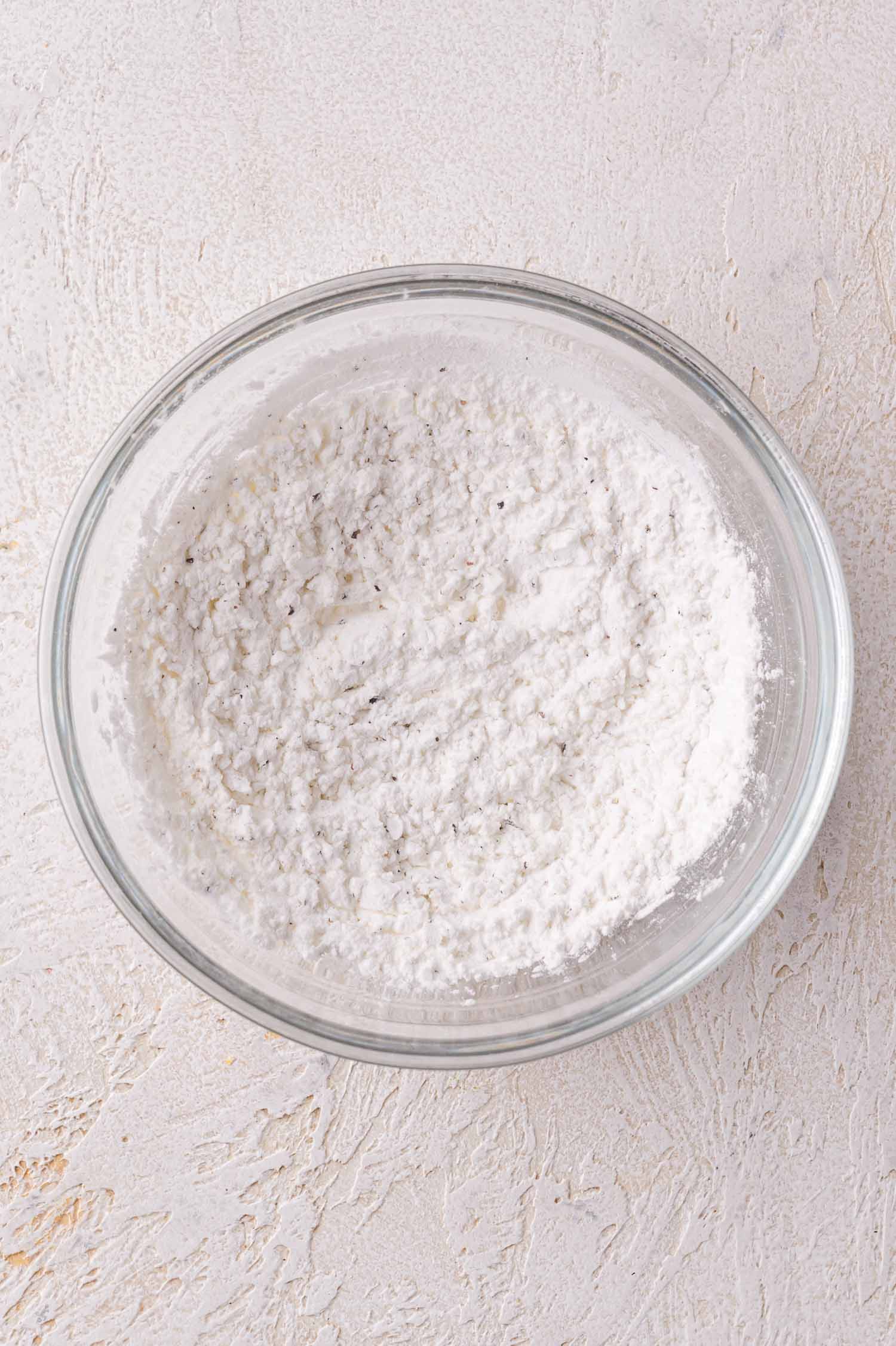 A clear glass bowl filled with a cornstarch mixture sits on a textured light-colored surface.