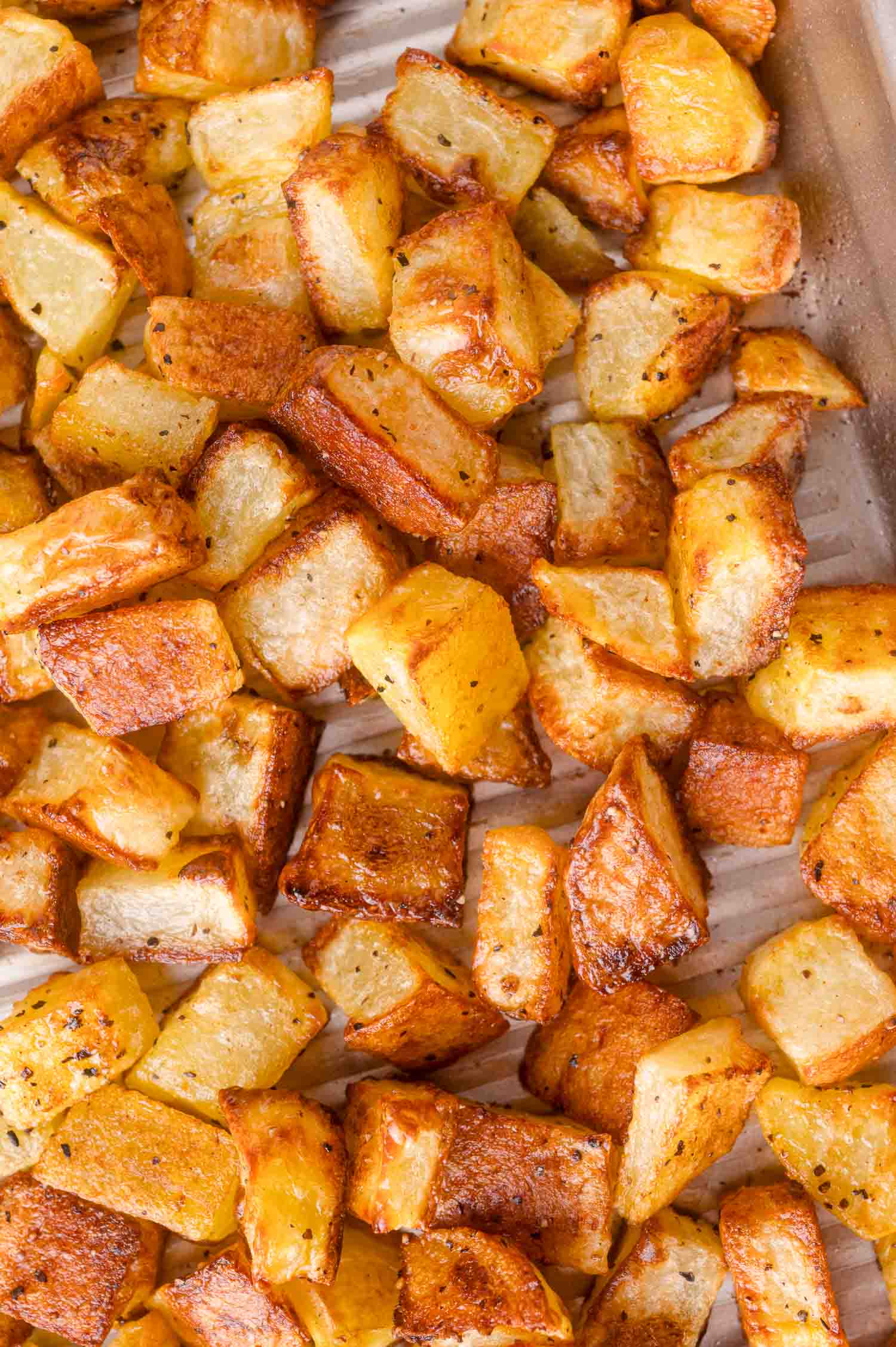 Close-up of golden brown roasted potato cubes on a baking tray, seasoned with pepper and salt.