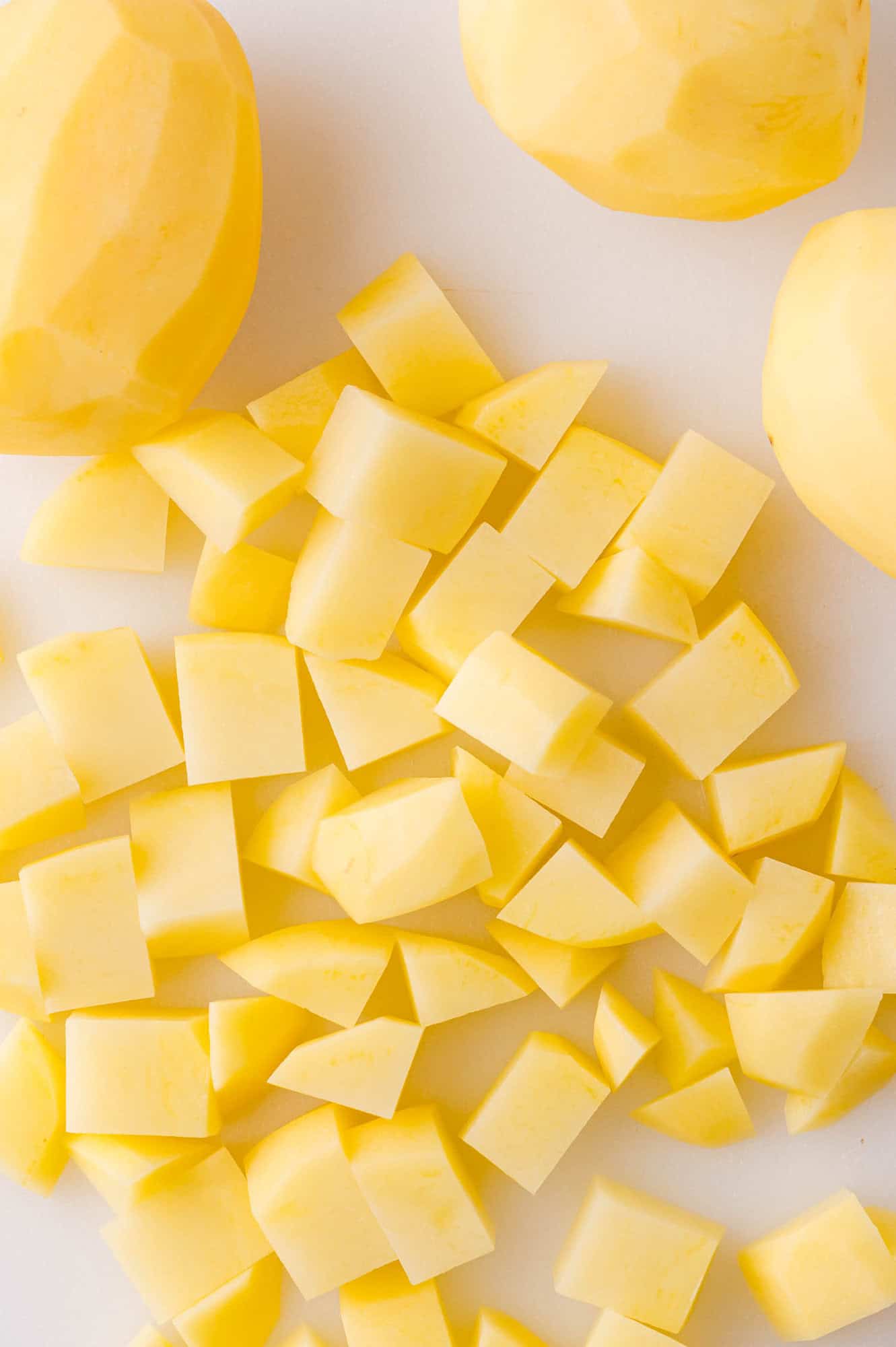 Peeled and diced yellow potatoes are arranged on a white surface.