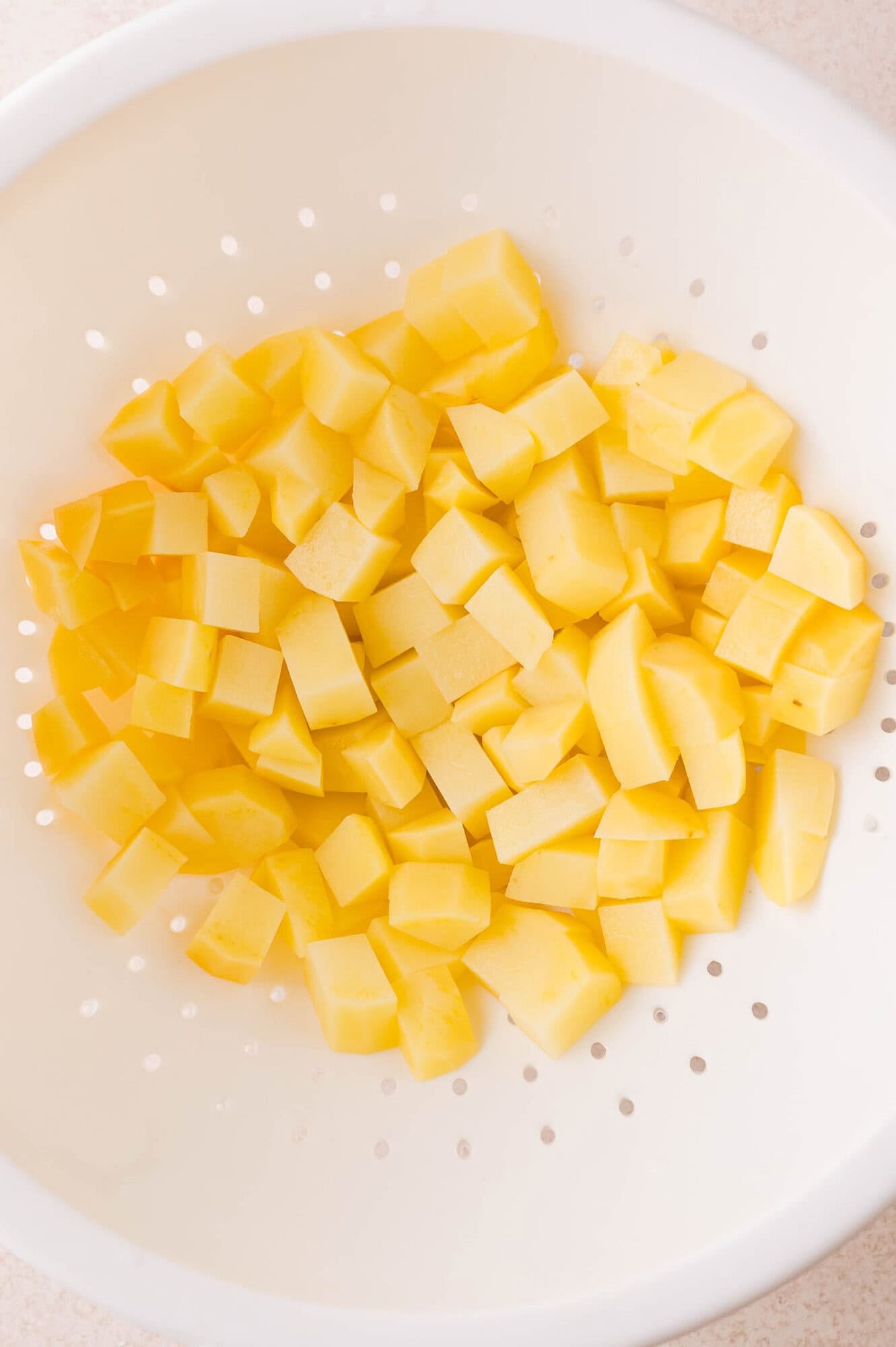 Diced yellow potatoes in a white colander.