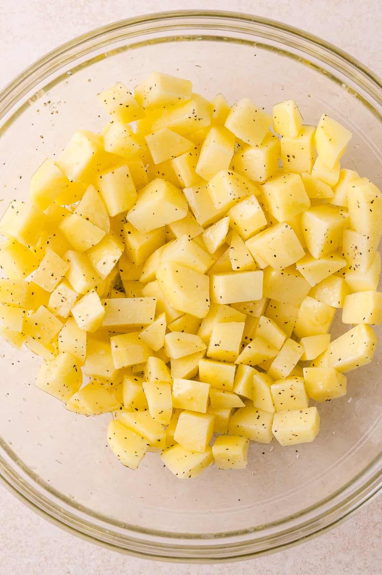 Diced raw potatoes seasoned with black pepper in a clear glass bowl.