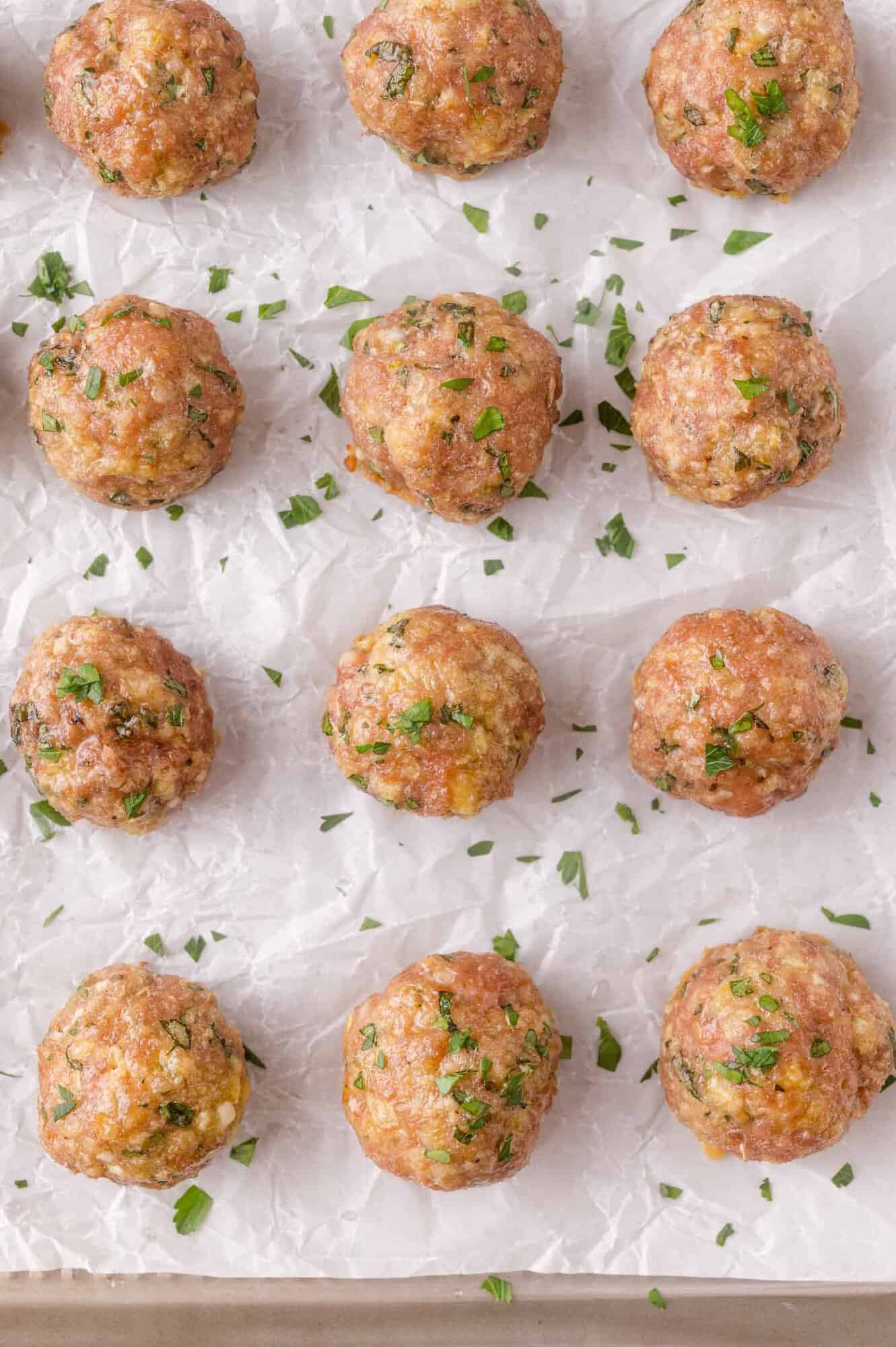 Twelve baked meatballs topped with chopped herbs are arranged on a sheet of parchment paper.