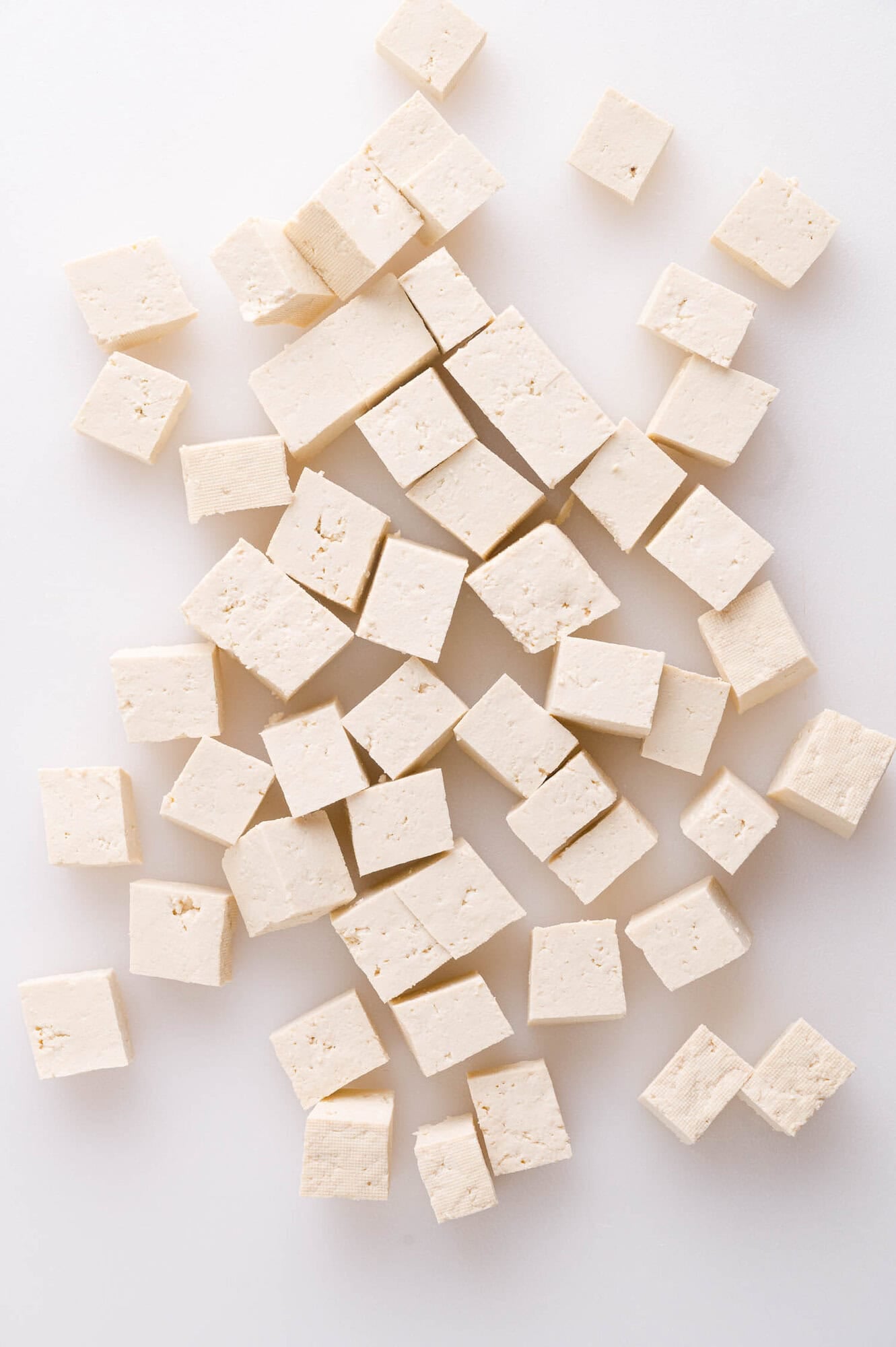 Cubed pieces of firm tofu scattered on a white surface.