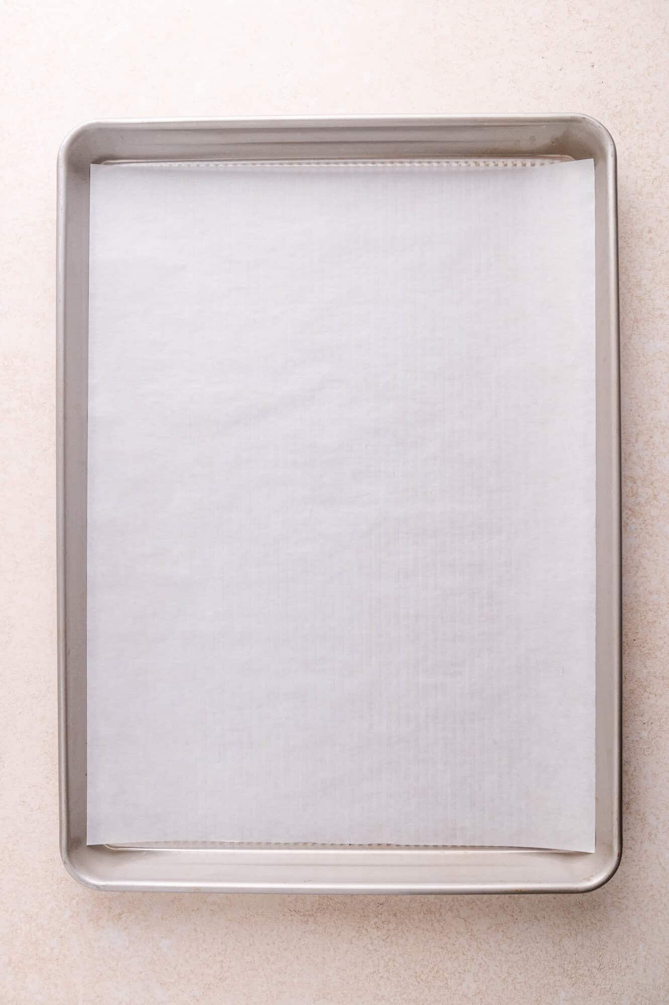 A baking sheet lined with a sheet of parchment paper on a light-colored surface.