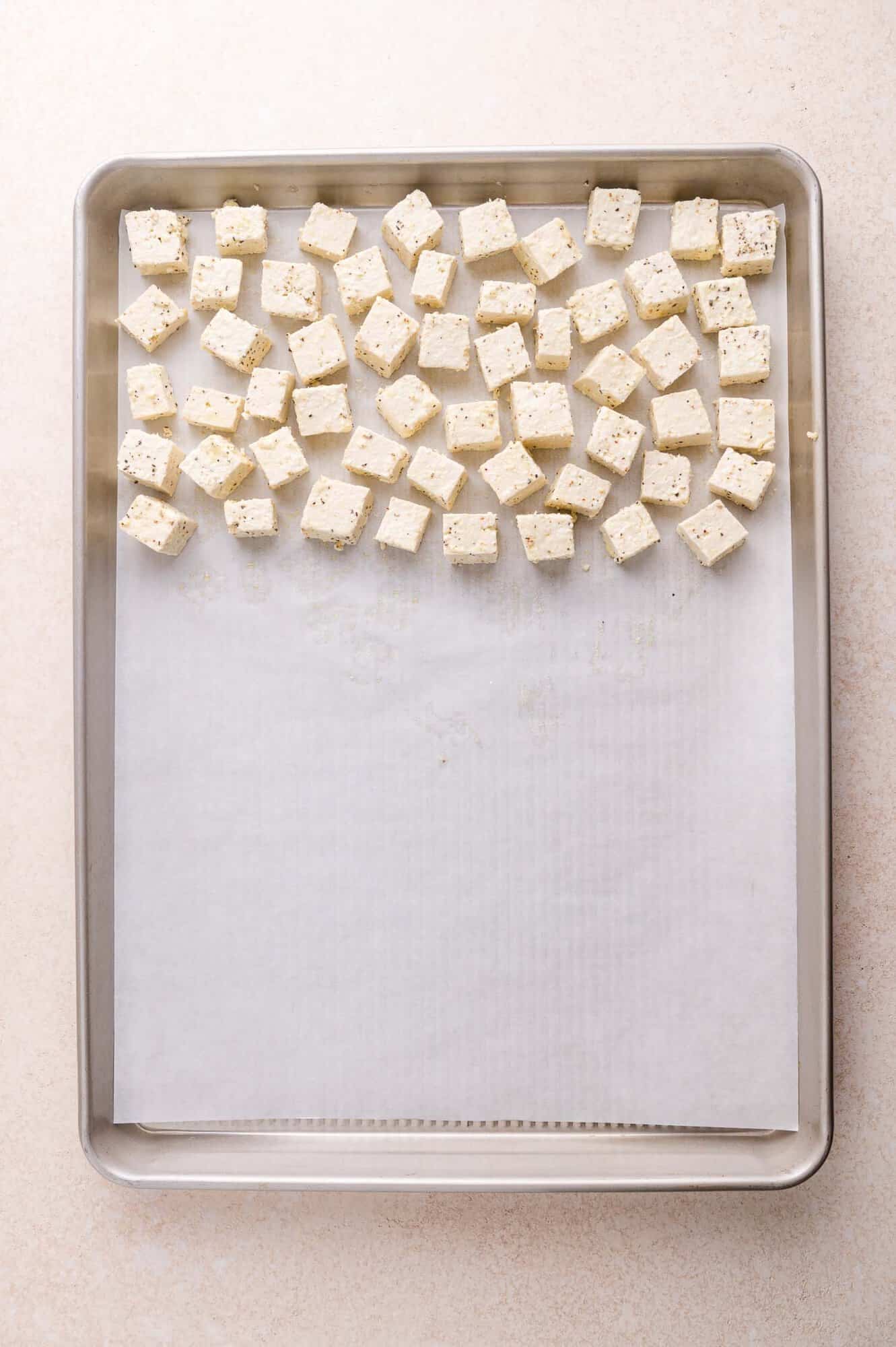 Cubes of seasoned tofu are arranged in a single layer on a parchment-lined baking sheet, ready for roasting.