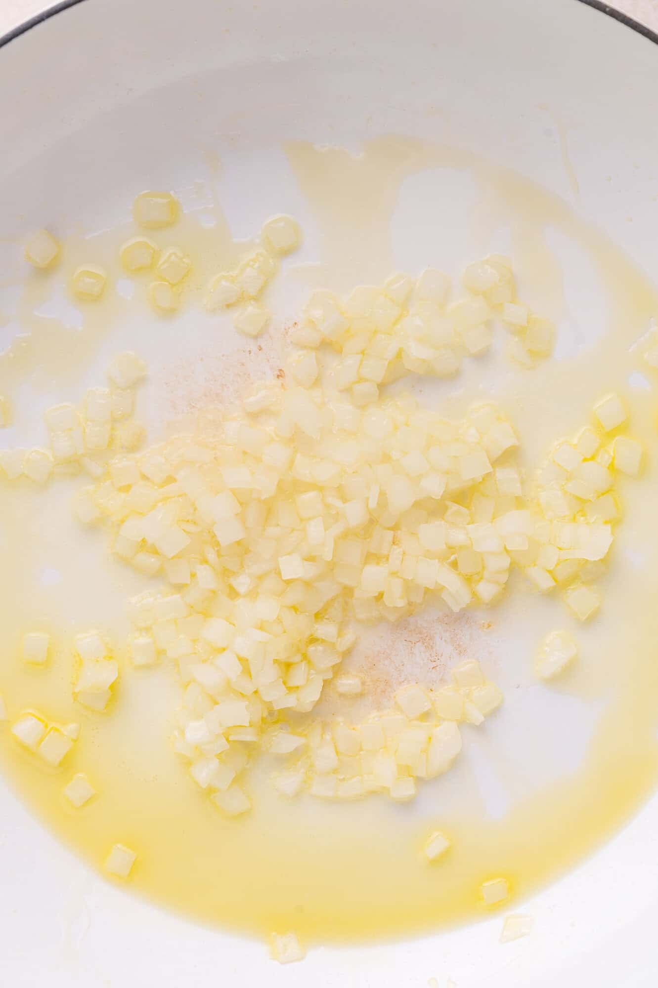 Diced onions cooking in oil in a white pan.