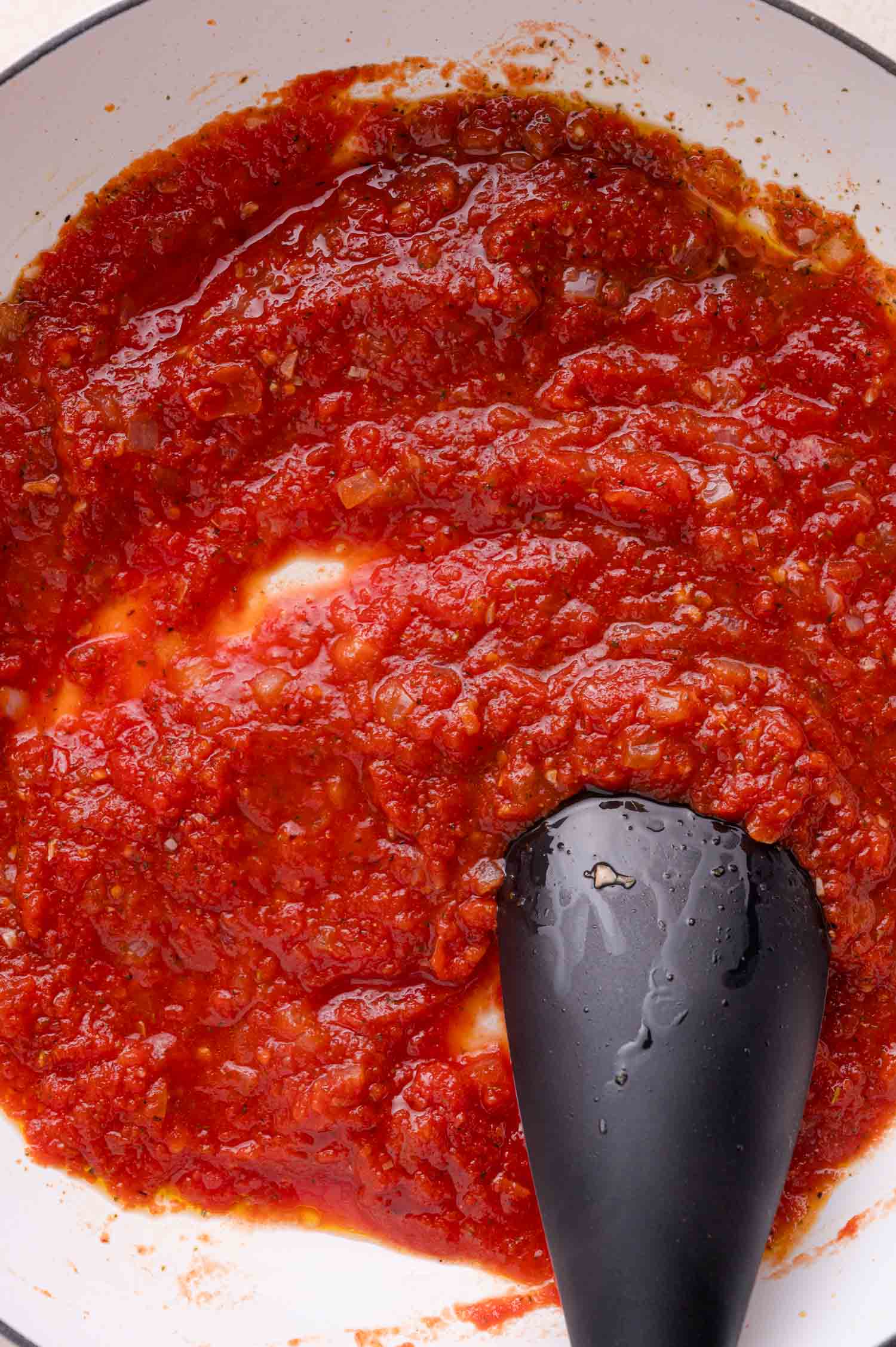 Tomato sauce being stirred in a white pan with a black silicone spatula.