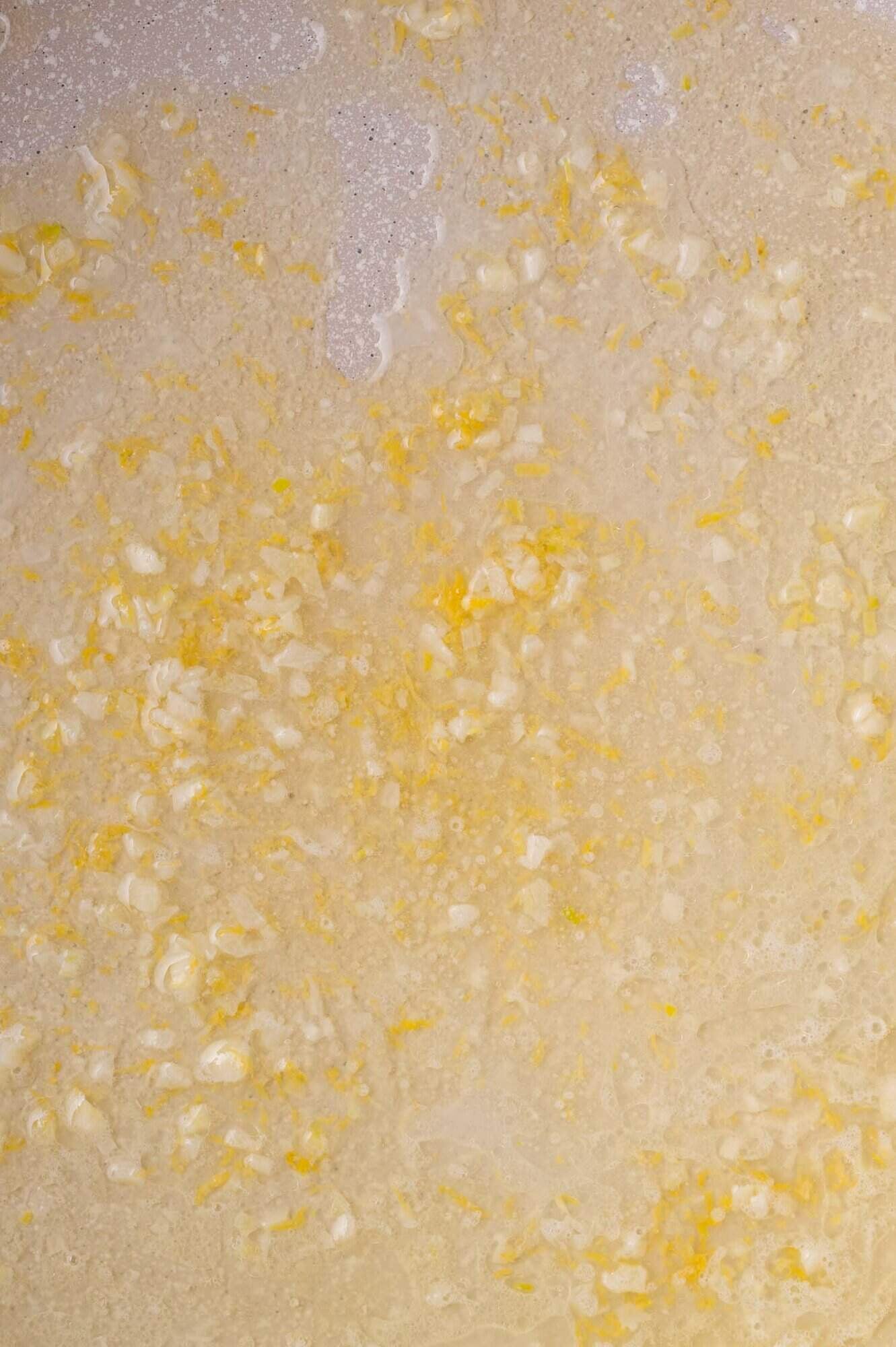 Chopped garlic and lemon zest sautéing in melted butter, seen from above.