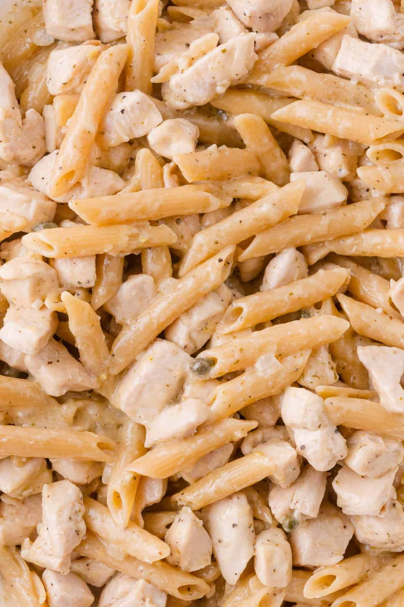Close-up of cooked penne pasta mixed with diced chicken in a creamy sauce.