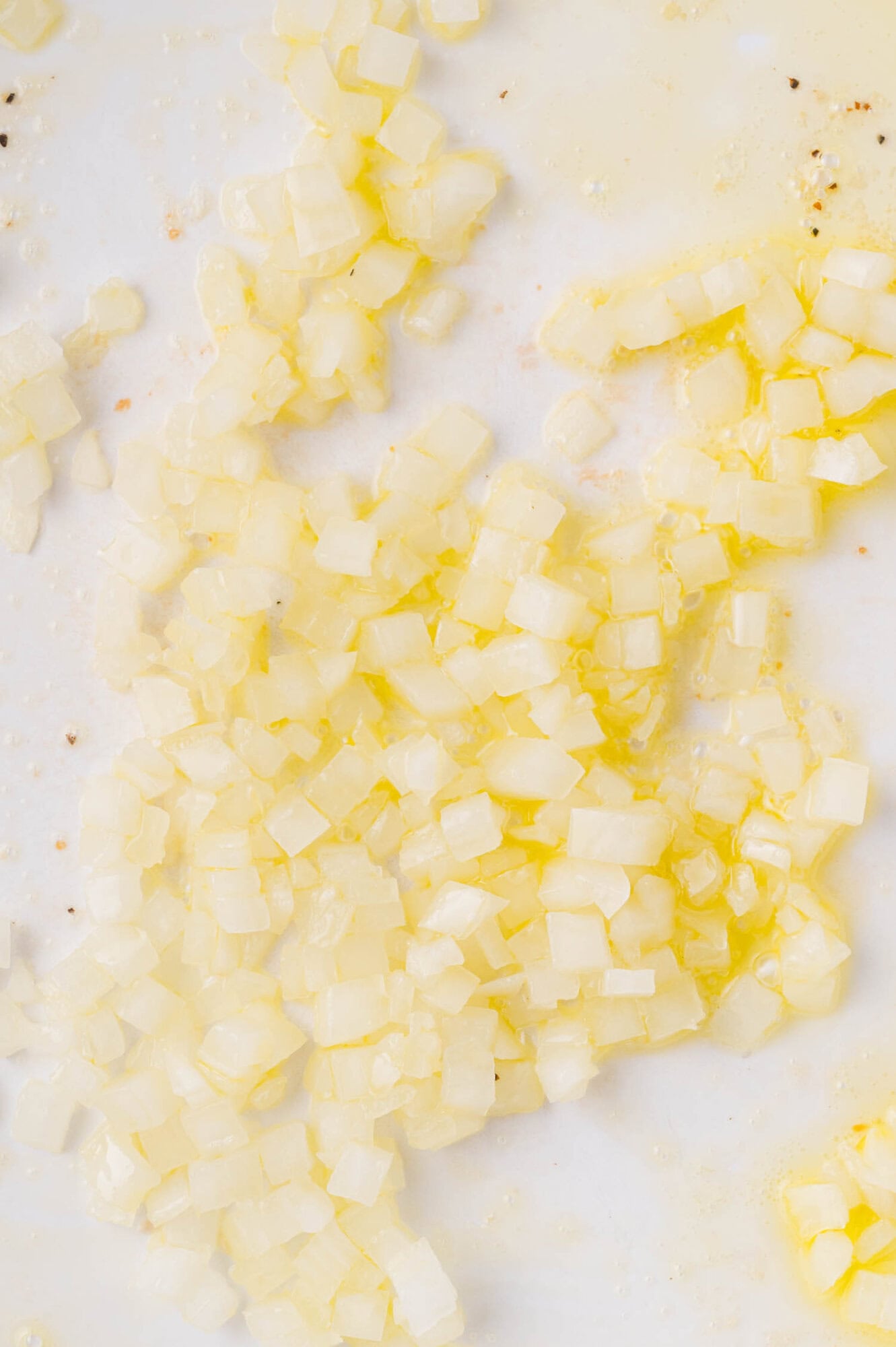 Diced onions being sautéed in oil in a white pan, with some pieces appearing translucent.