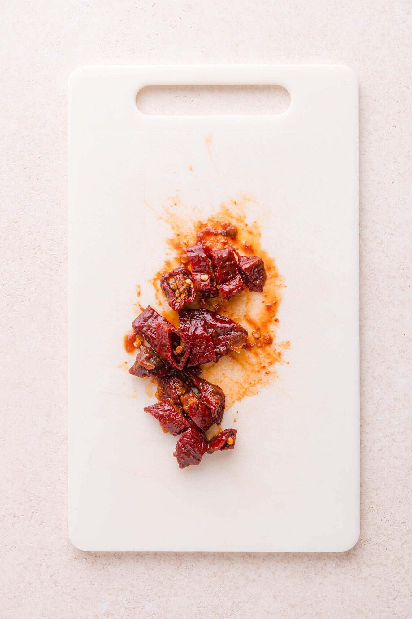 Chopped chipotle peppers on a white cutting board placed on a light-colored countertop.