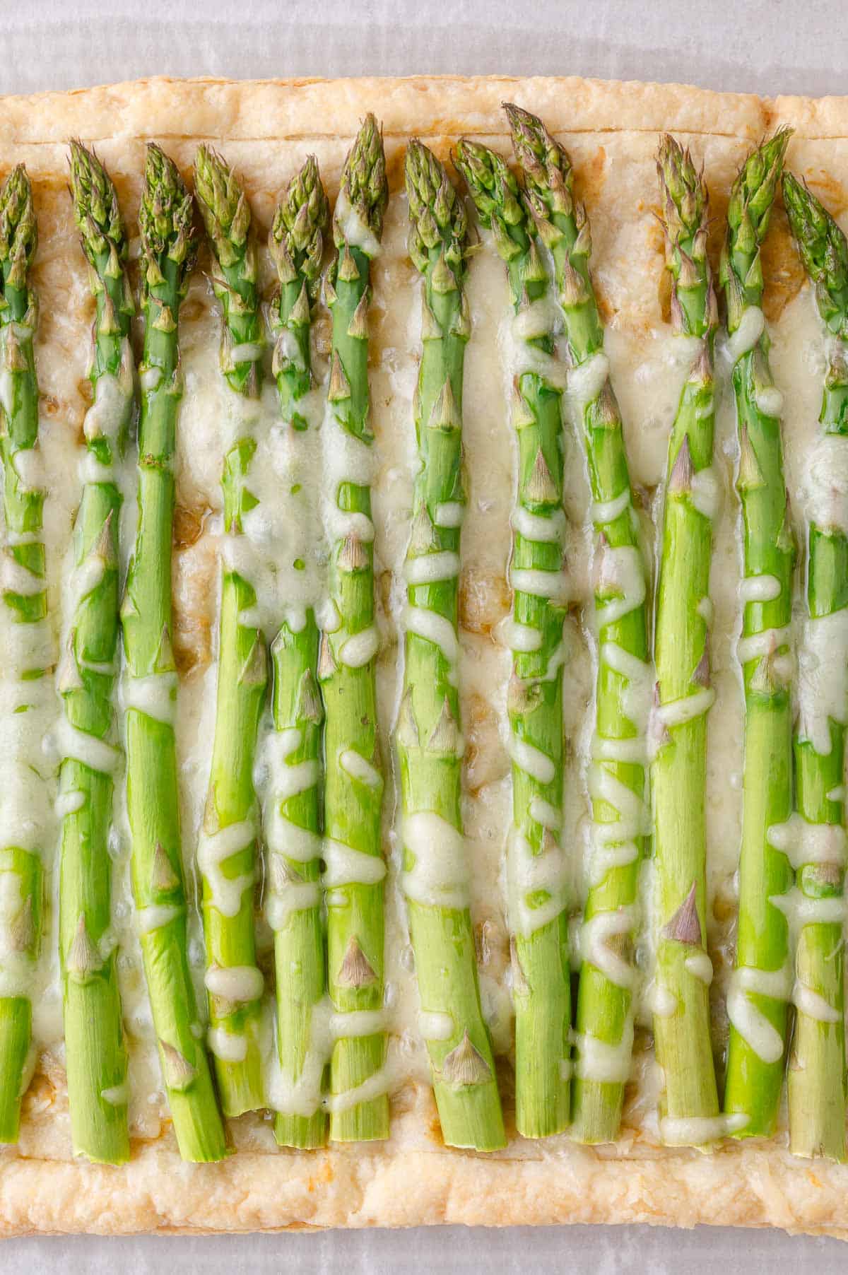 A rectangular tart topped with whole asparagus spears and melted cheese on a layer of puff pastry.