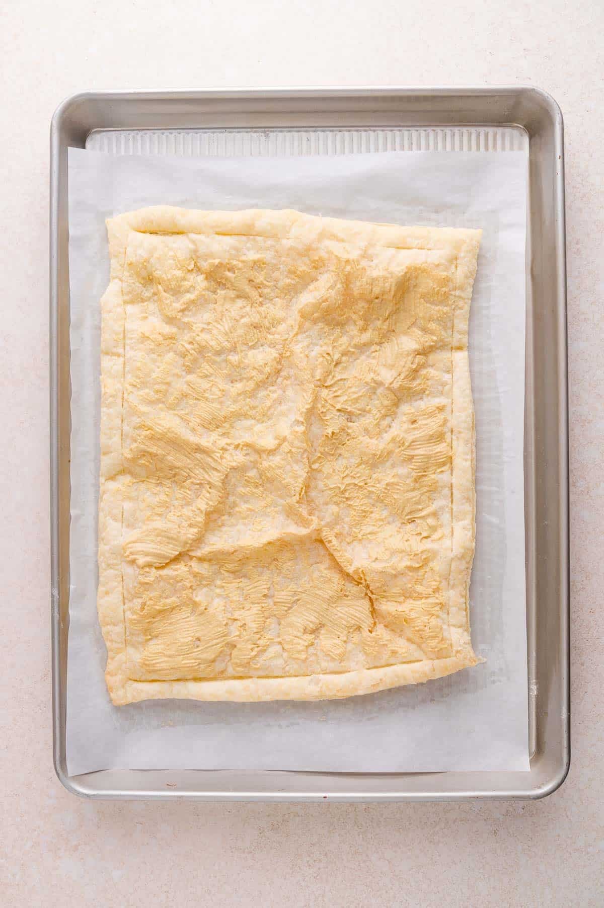 A sheet of baked puff pastry sits on parchment paper on a metal baking tray.