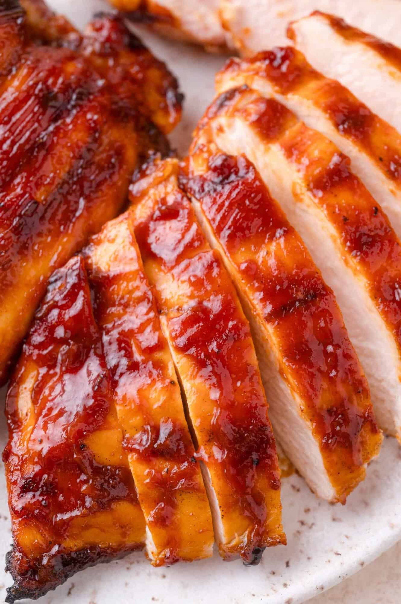 Sliced, glazed barbecue chicken breast arranged on a white plate, showing a caramelized, glossy surface.
